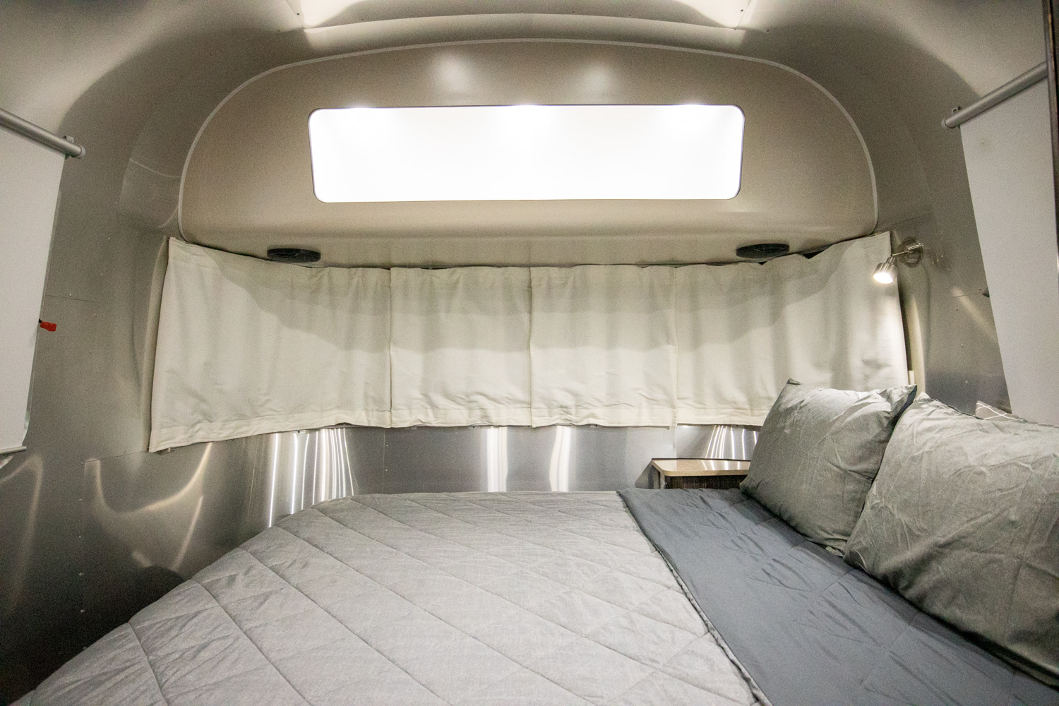 Interior of a modern rv rental bedroom featuring a comfy gray bed, metallic walls, and a bright overhead skylight.. Airstream International 2018