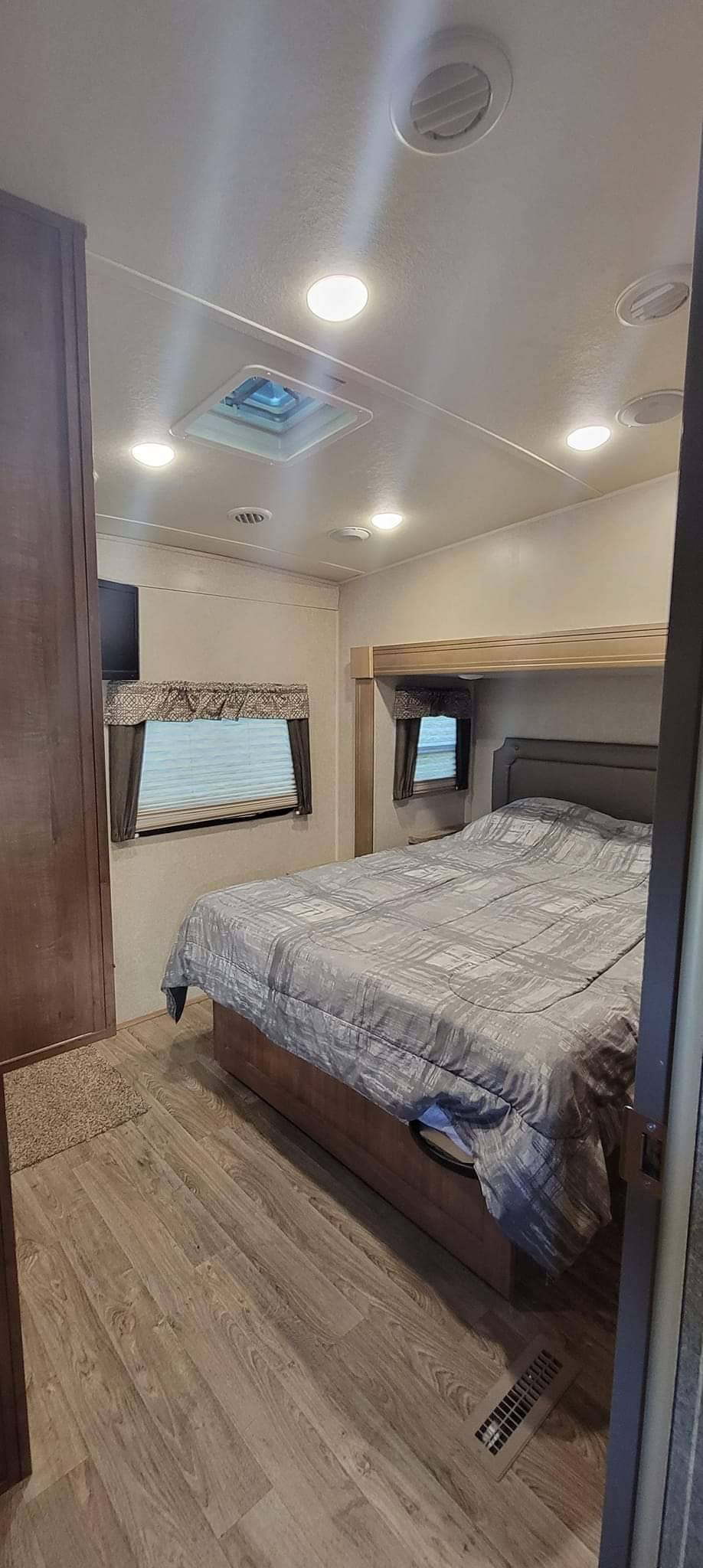 This RV rental bedroom offers a comfortable bed, wood laminate floors, windows, ceiling vents, and a skylight.. Forest River Flagstaff Super Lite 2018