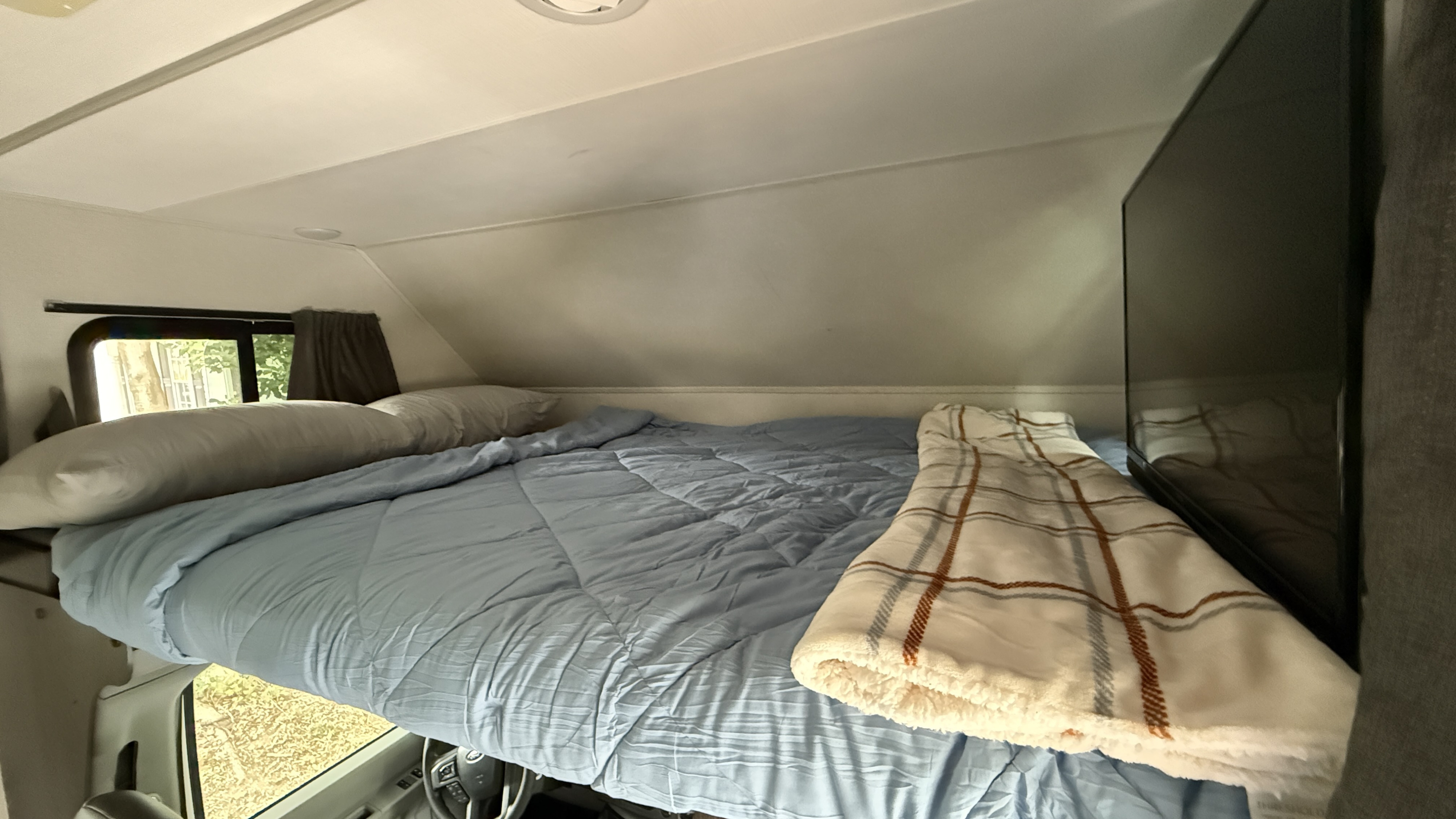 Inside an RV rental: a comfortable overhead bunk bed with light blue bedding, a TV, and a window.. Forest River Sunseeker LE 2023