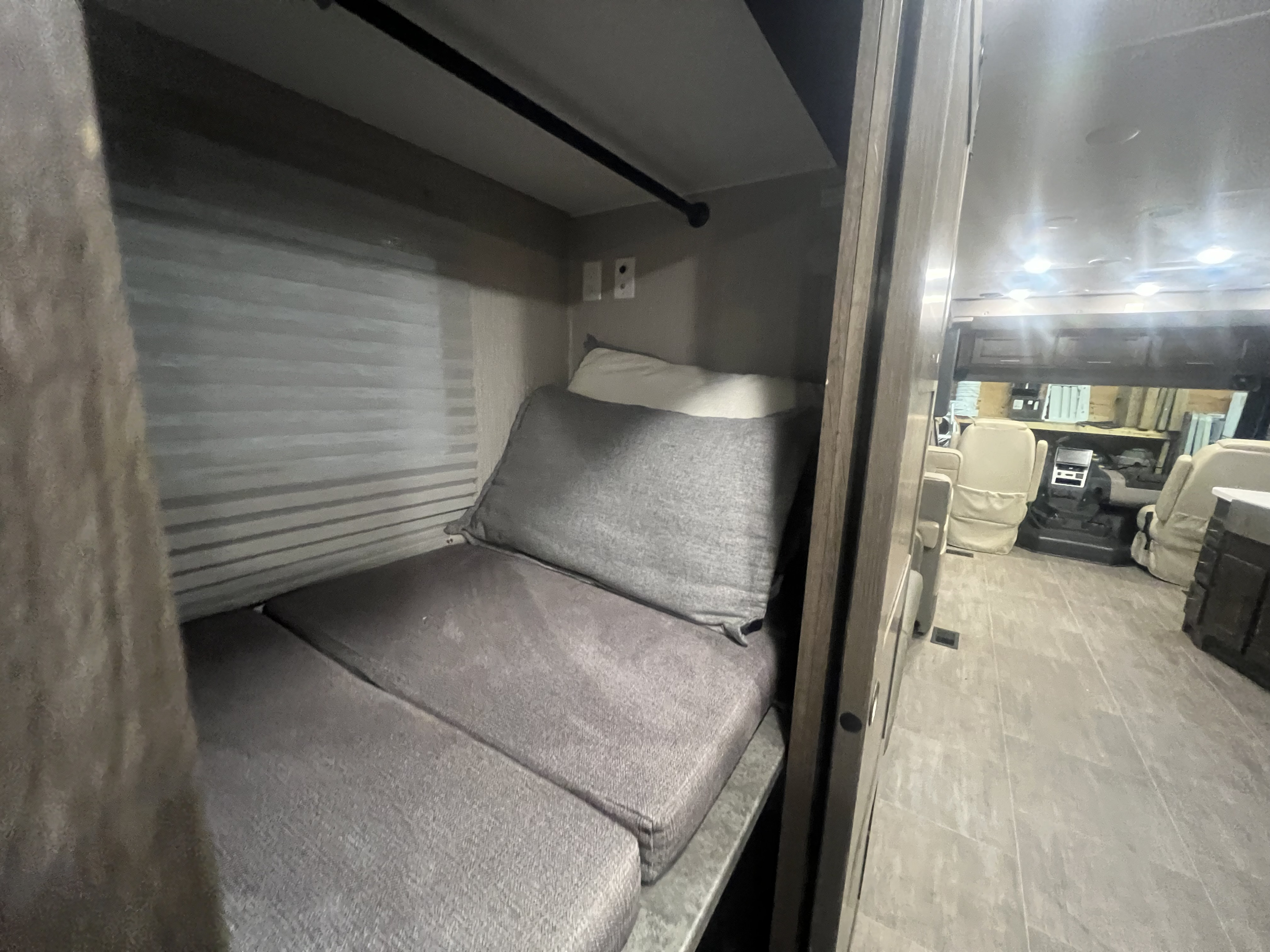 Cozy bunk bed in an RV rental, featuring gray cushions, with a view of the vehicle's front cockpit and swivel seats.. Forest River Coachmen Mirada 2022