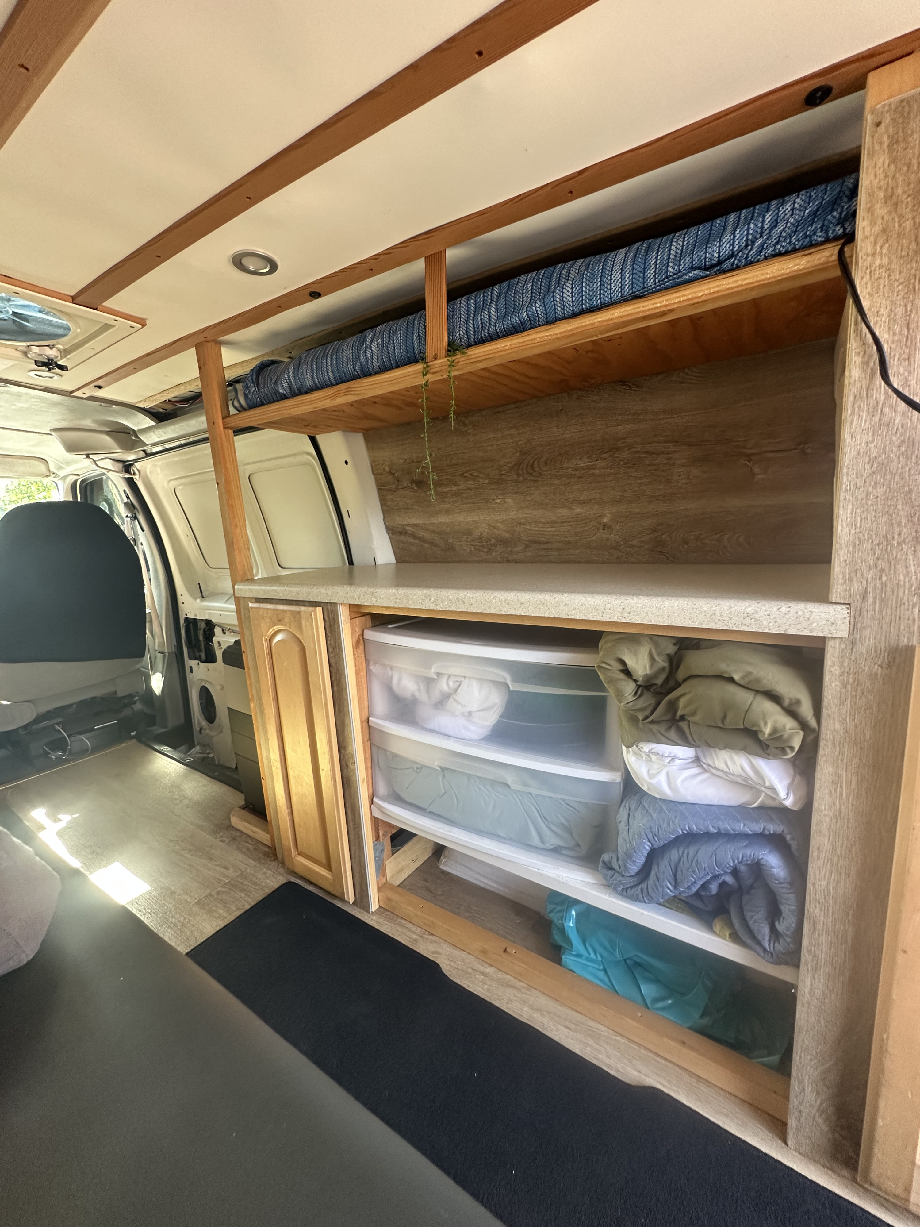 This RV rental showcases a functional van interior with custom wood shelving, a compact bed, a countertop, and clear storage drawers.. Ford Econoline 150 2005