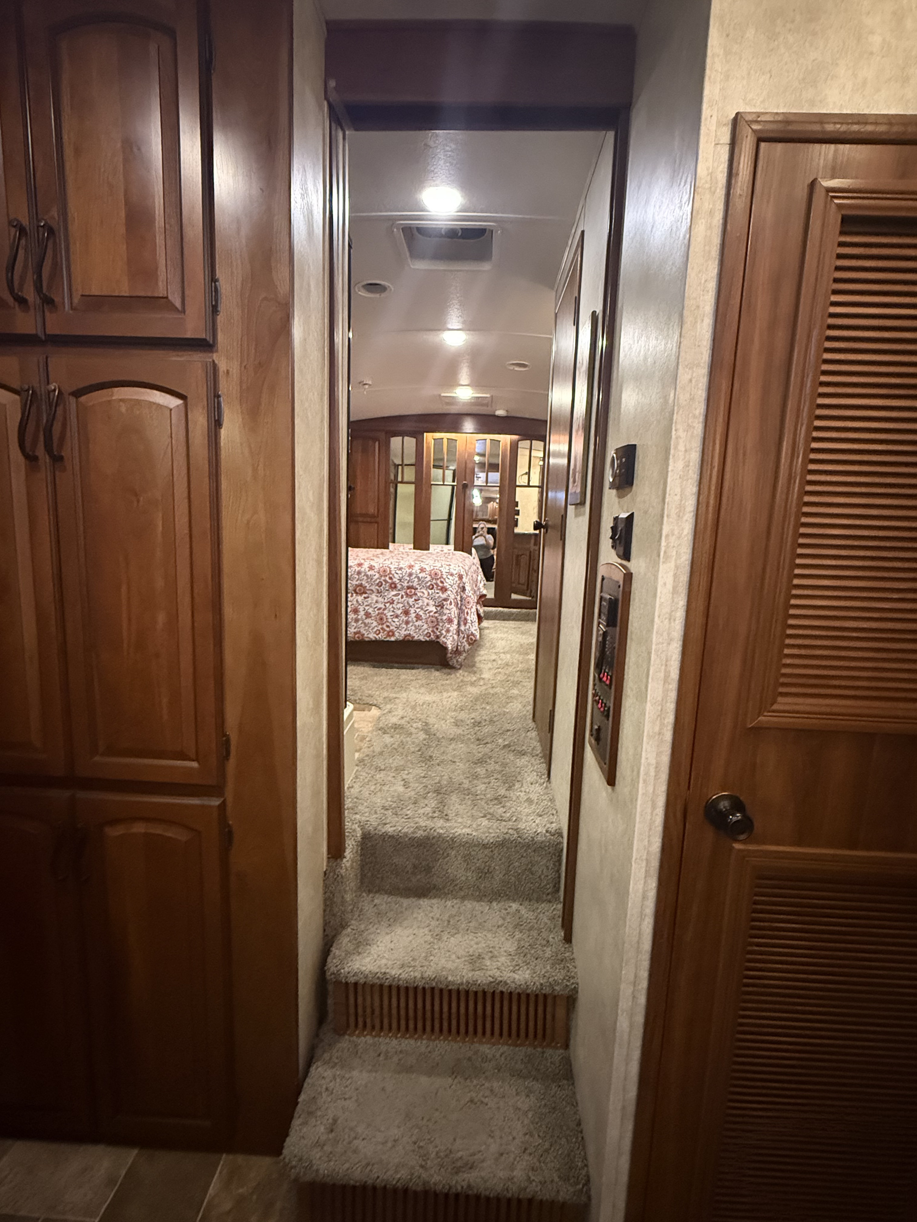 Inside an RV rental, a carpeted hallway with steps leads to a bedroom. Features wood cabinets, controls, and warm lighting.. Keystone RV Montana Hickory 2013