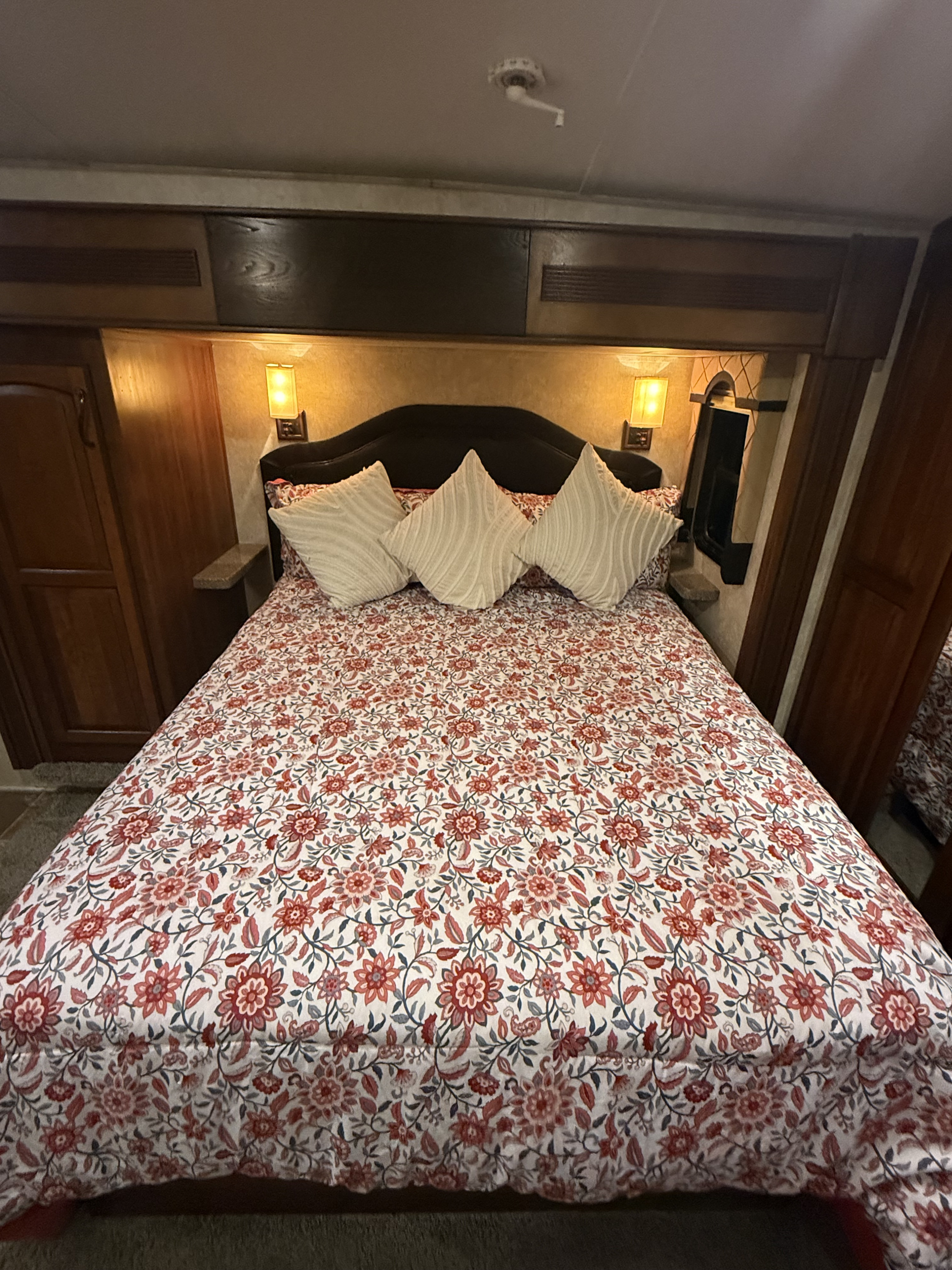 An RV rental bedroom with a comfy bed, striking floral comforter, and warm bedside lighting, perfect for a cozy stay.. Keystone RV Montana Hickory 2013