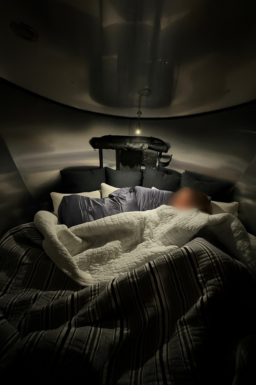 Enjoy a comfortable sleep in this **rv rental** interior. A person rests under a quilted blanket, perfect for your next camping trip.. Airstream Basecamp 2025