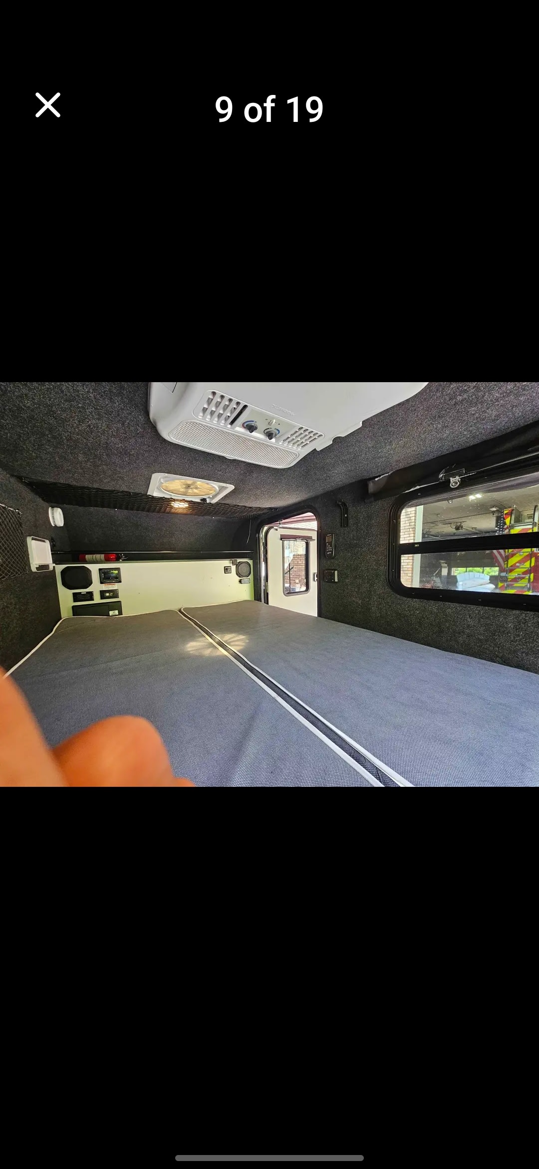 Inside this RV rental: a spacious gray bed, dark upholstered interior with AC, fan, controls, and a window view.. InTech RV Flyer 2022