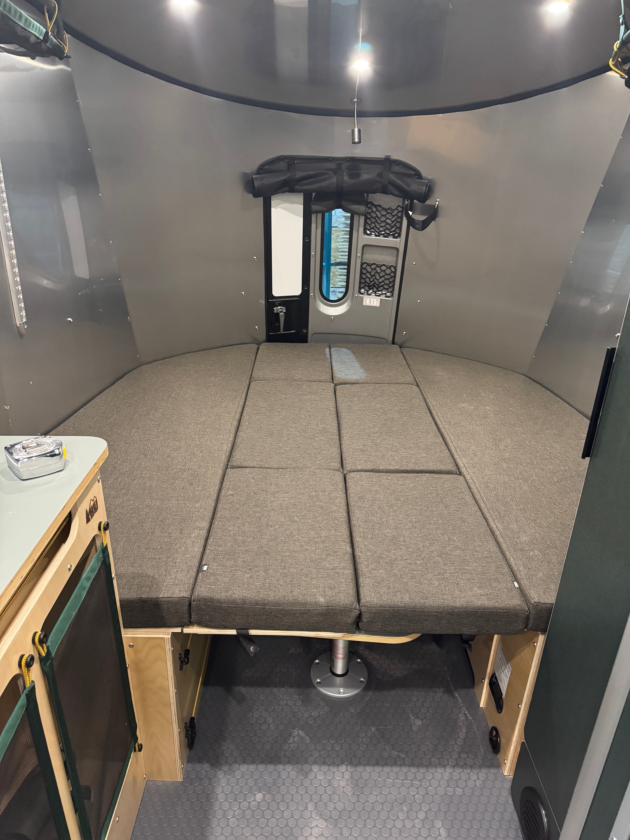 Cozy RV rental interior: segmented bed, small counter, under-bed storage, and rear window in a compact camper.. Airstream Basecamp 2025