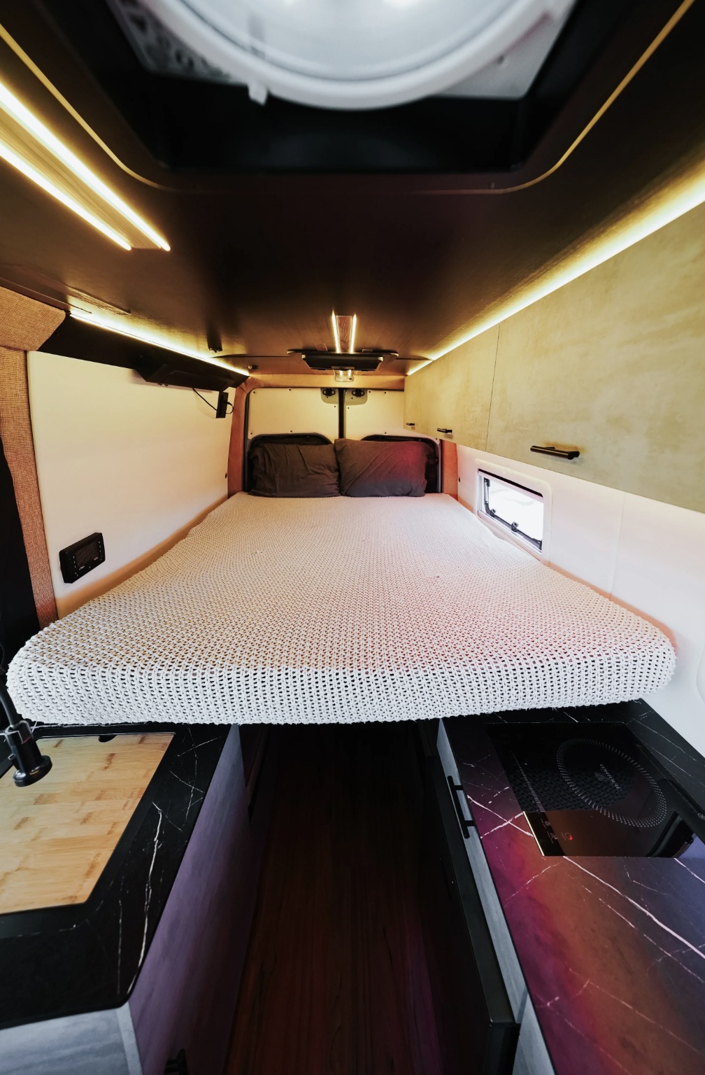 Explore this modern rv rental interior! Featuring a spacious bed, integrated kitchen with cooktop, and ambient lighting in a cozy camper van.. Other Mercedes Sprinter 2025
