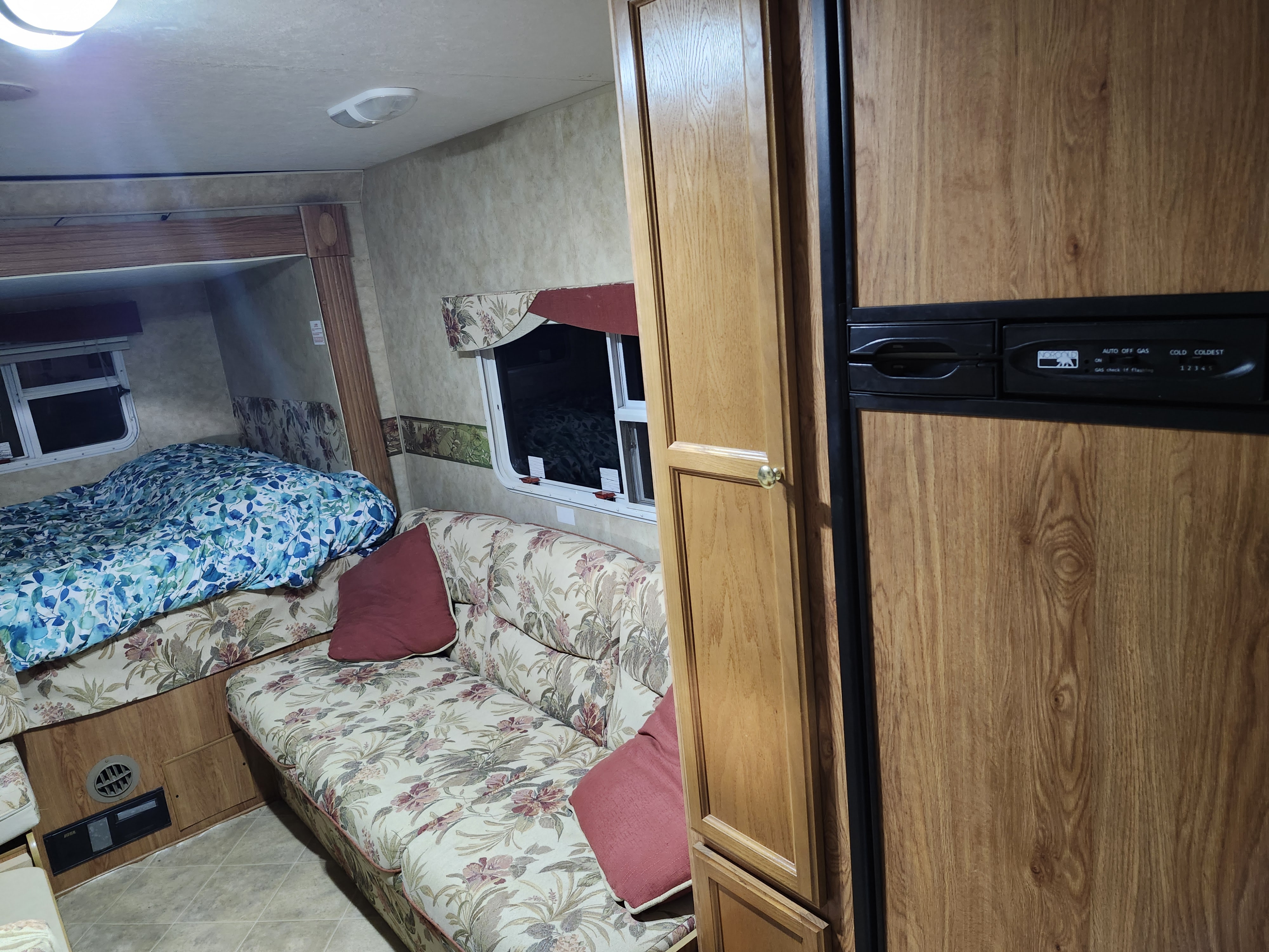 This cozy rv rental interior features a bed with blue floral bedding, a patterned sofa, and wood cabinetry with a fridge.. Jayco Jay Feather EXP 2008