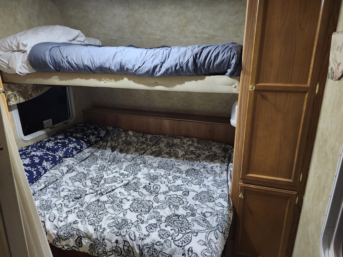 Cozy RV rental bunk beds with patterned bedding and a wooden cabinet, offering a comfortable sleeping area for travelers.. Jayco Jay Feather EXP 2008
