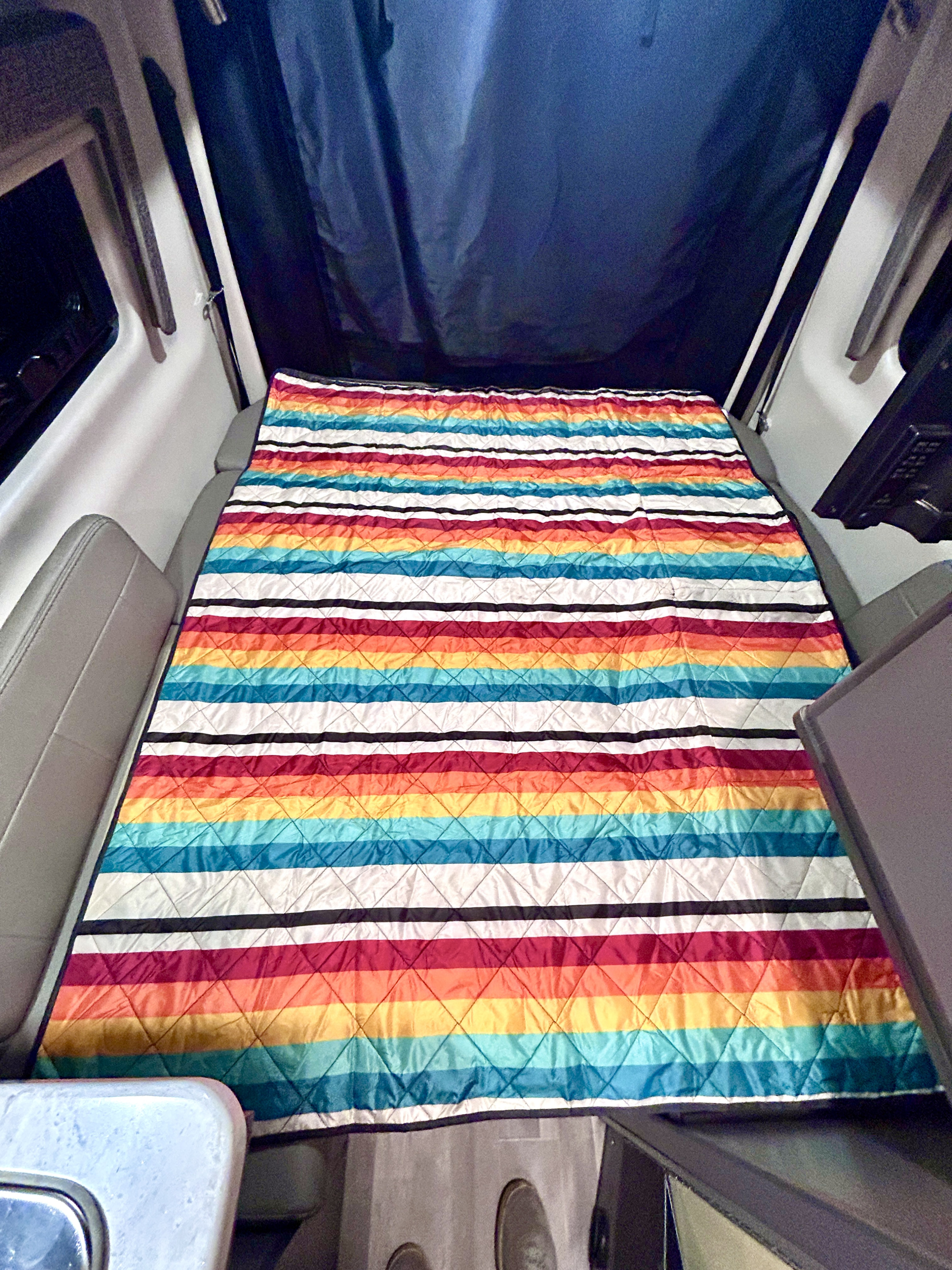 Enjoy the vibrant comfort of this rv rental bed, featuring a quilted, rainbow-striped blanket within a modern interior.. Thor Synergy 2022