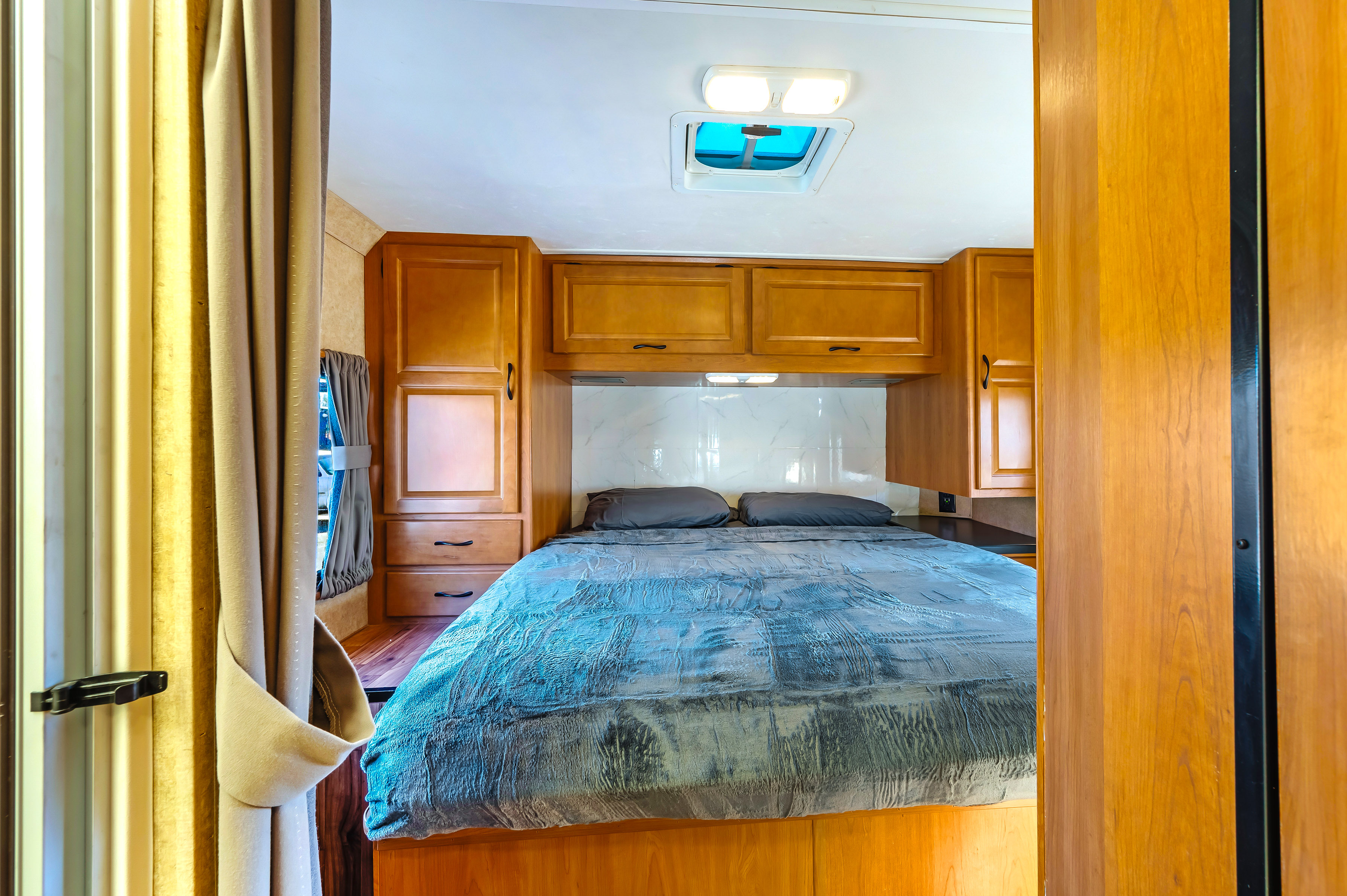 Cozy RV rental bedroom with a comfortable bed, overhead cabinets, and a skylight, offering a compact, functional space.. Thor Majestic 2017
