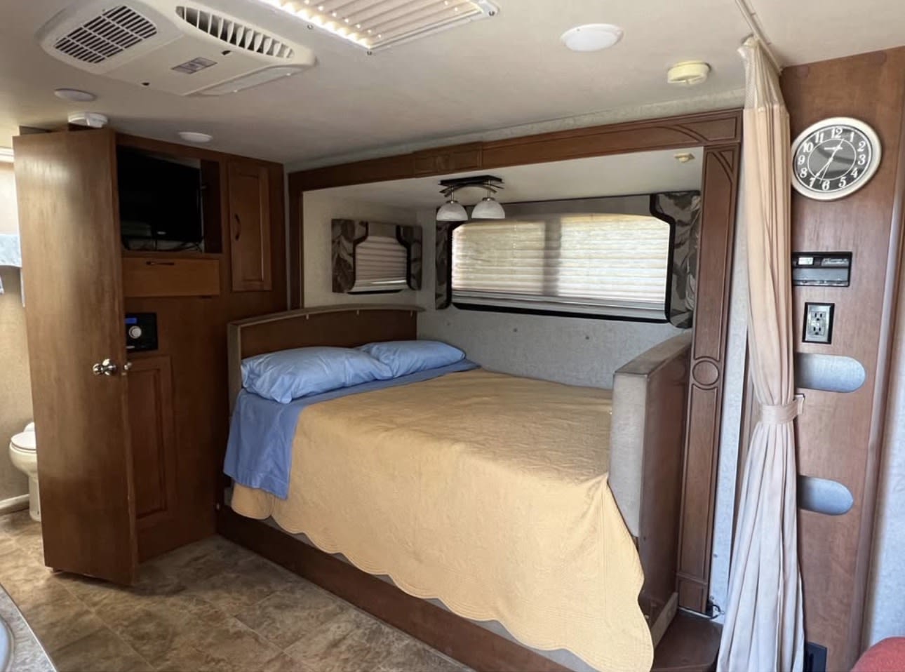 This inviting RV rental bedroom features a cozy bed, mounted TV, window, AC unit, and visible bathroom access on the left.. Lance Manufacturing Lance Manufacturing Trailer 2016