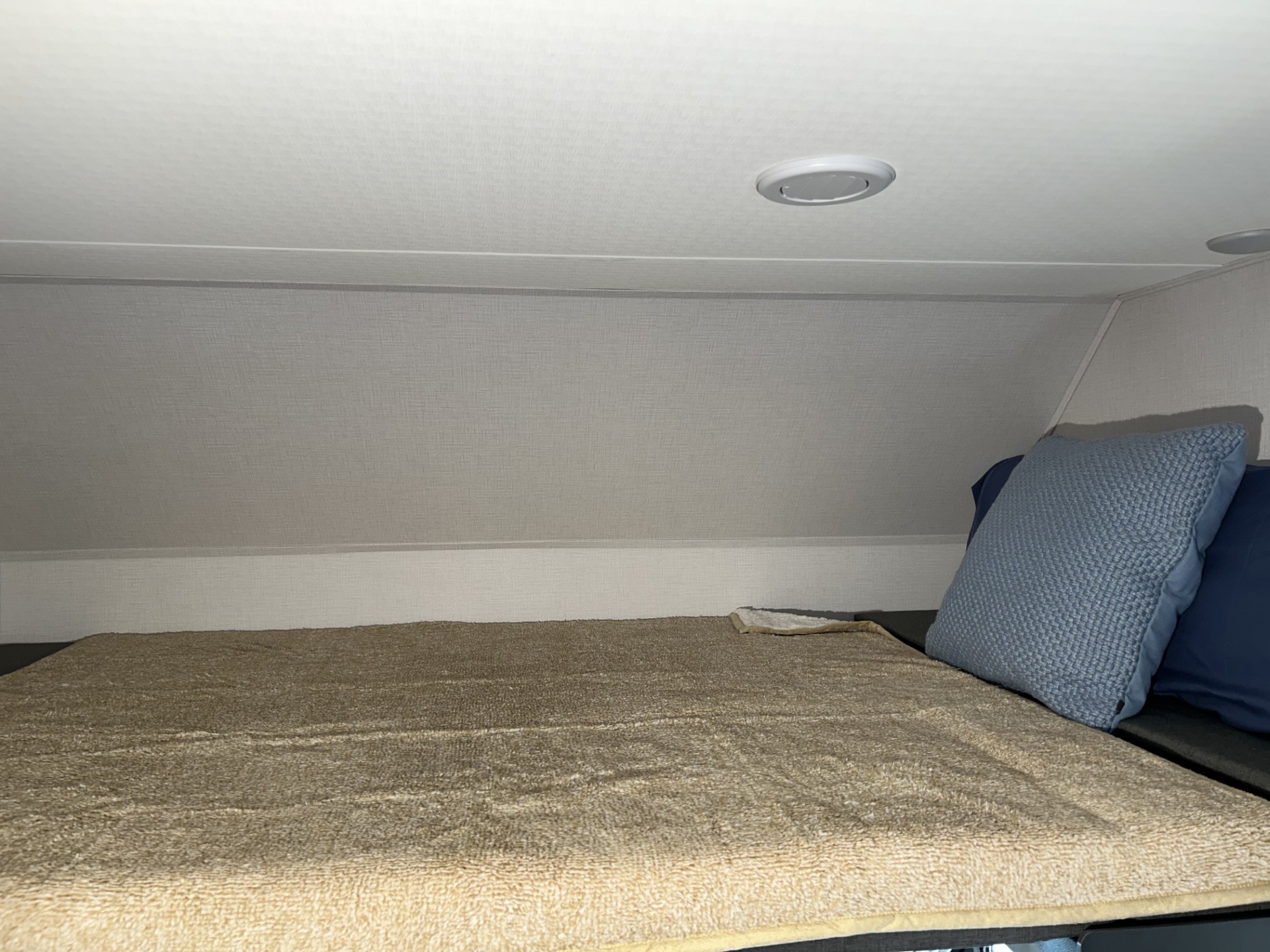 Cozy RV rental bunk bed with a light brown blanket, blue pillows, and recessed overhead lighting in a compact sleeping area.. Forester LE 2026