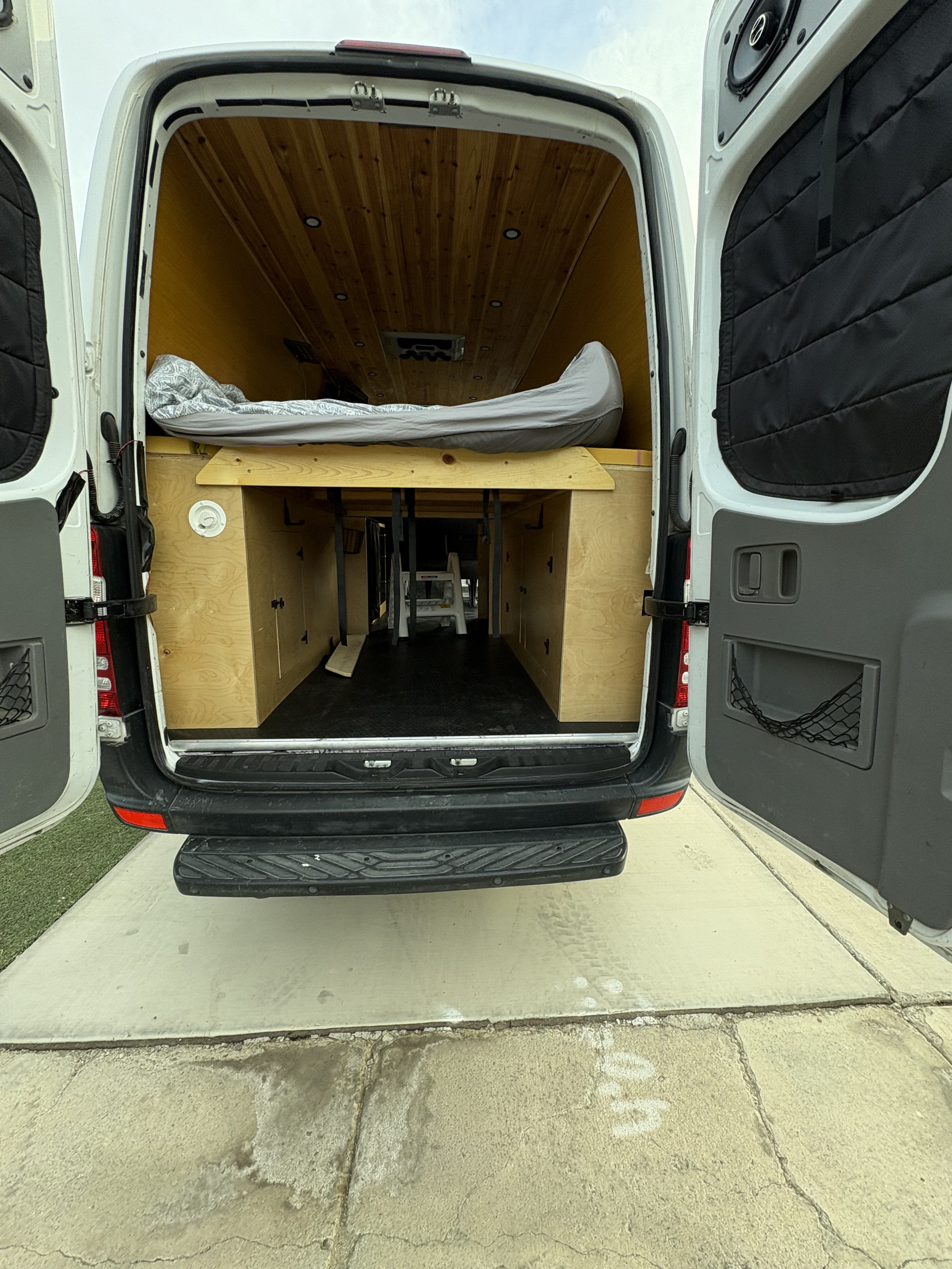 Rear view of an RV rental camper van's custom wood interior, featuring a raised bed and ample storage for adventures.. Mercedes Sprinter 2010