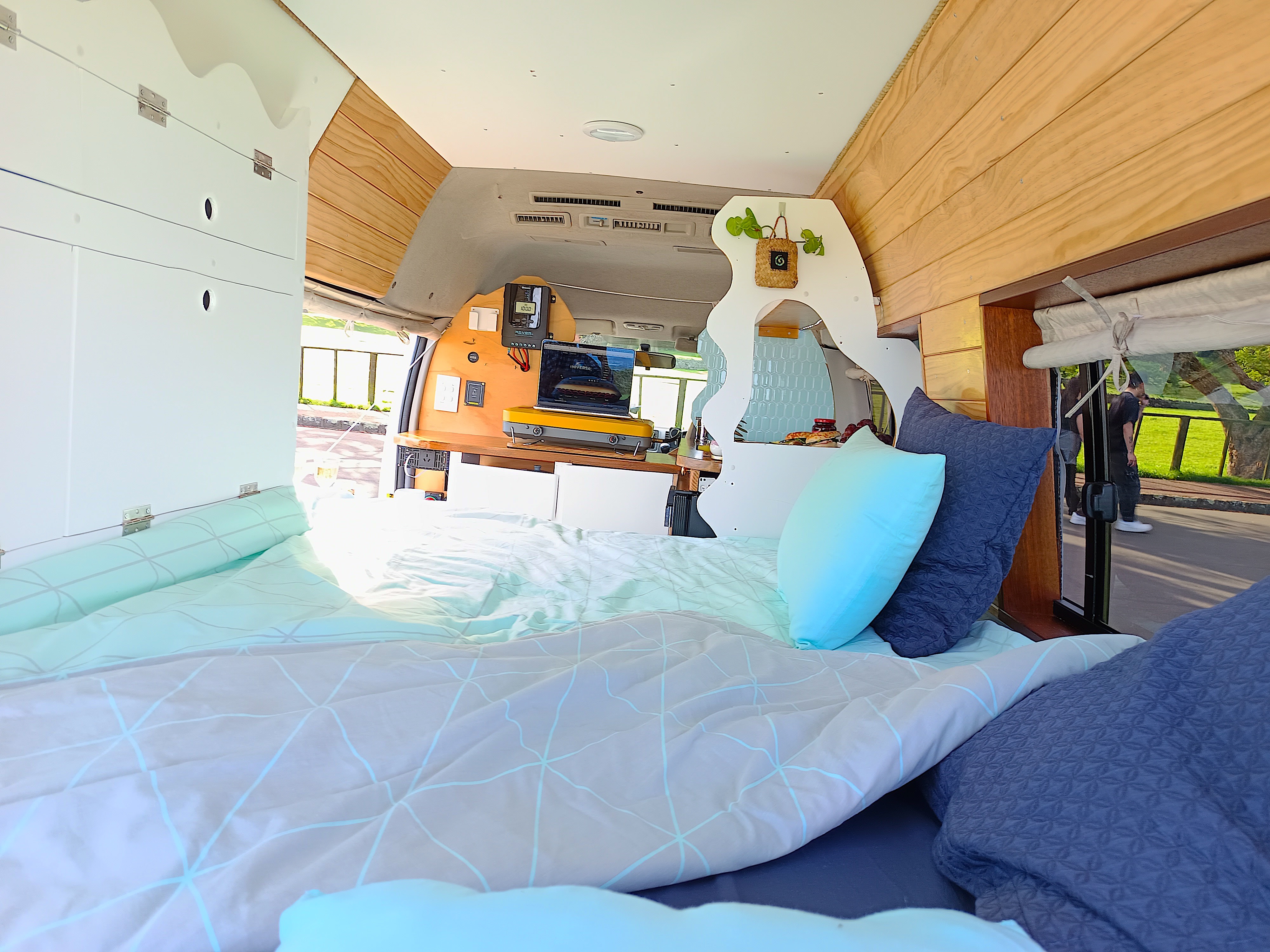 Cozy rv rental interior: view from the bed with blue bedding, wood walls, and a compact kitchen/workspace at the front. Ready for trips.. Toyota Hiace 2005