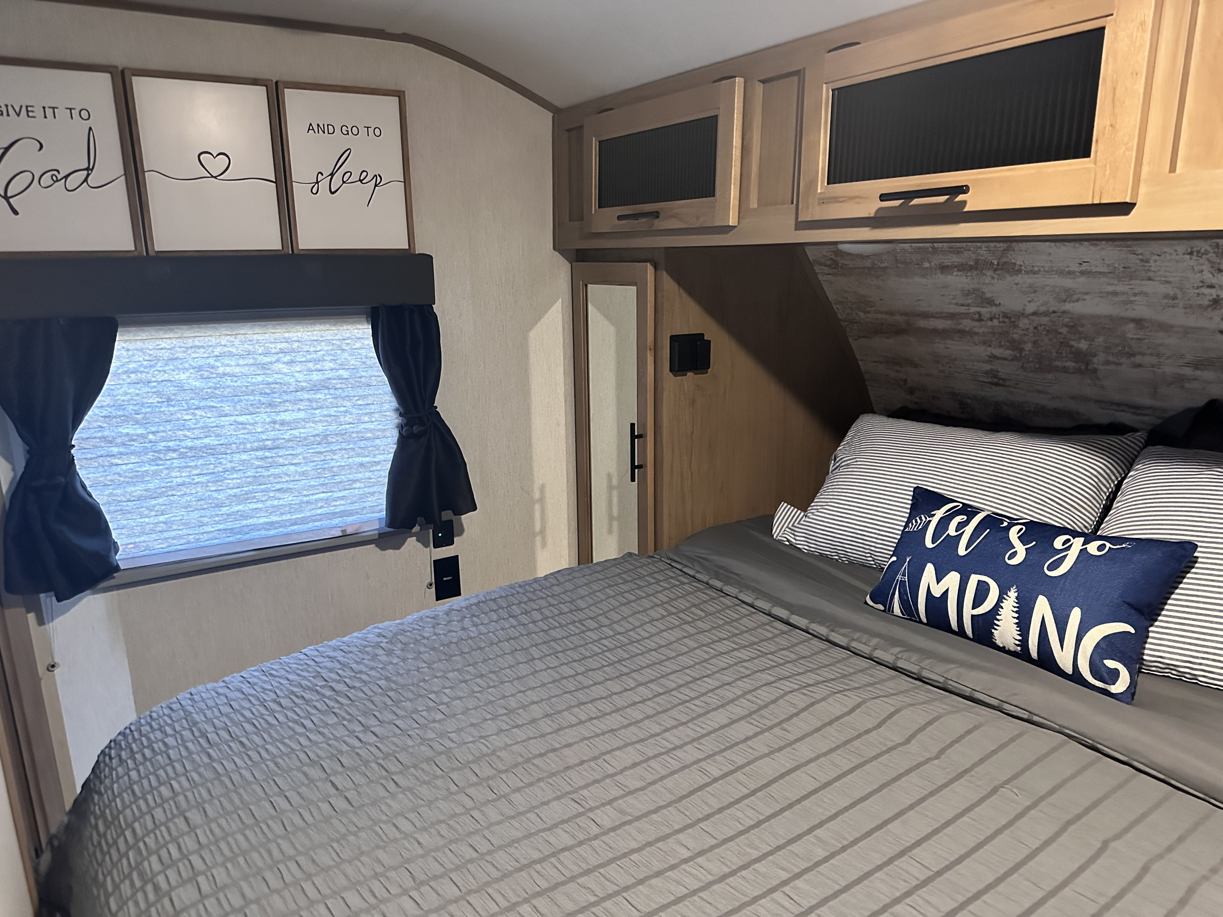 Cozy RV rental bedroom featuring gray bedding, a "Let's Go Camping" pillow, and inspirational wall art.. Forest River Cherokee Alpha Wolf 2023
