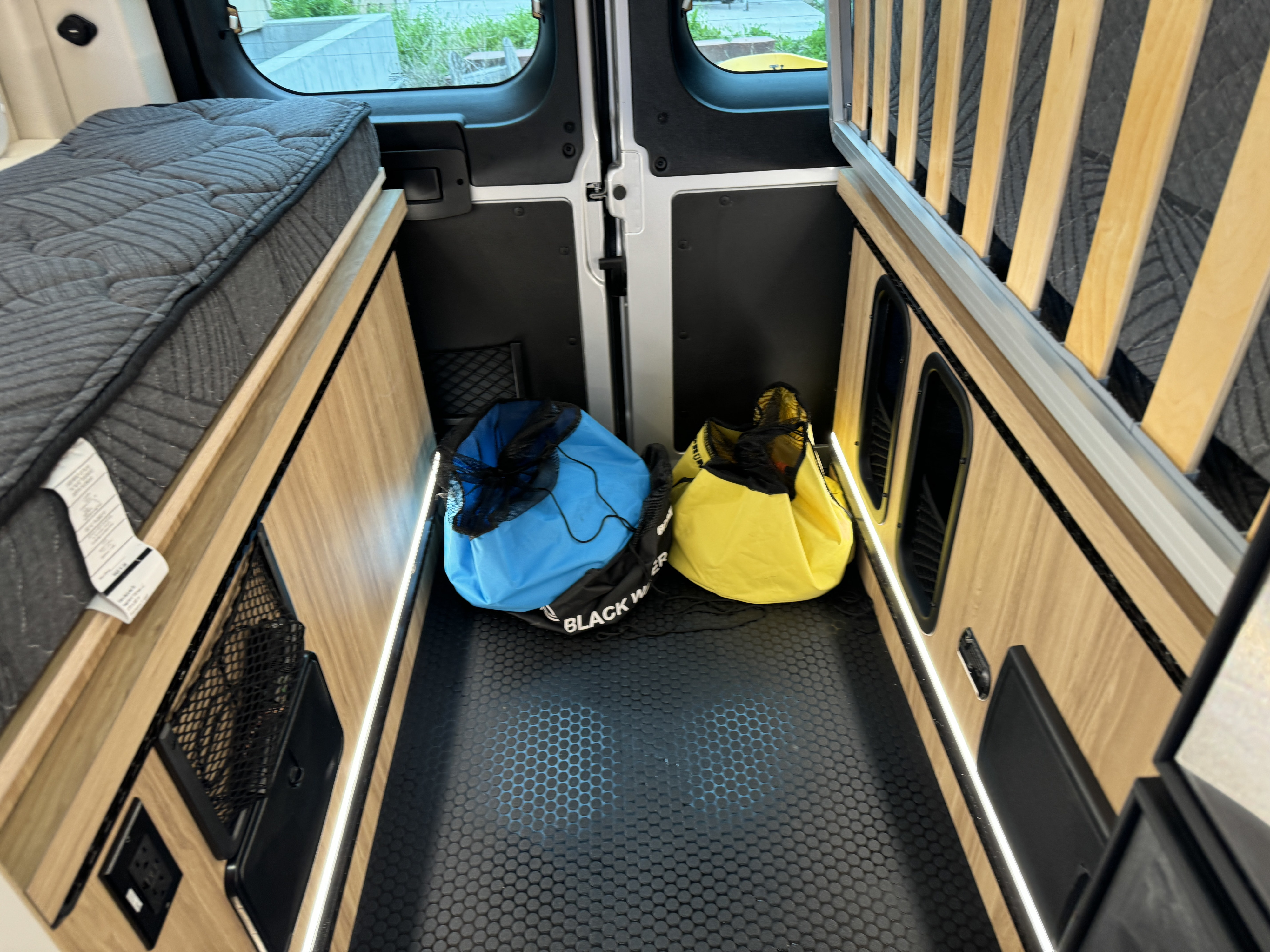RV rental storage: Under-bed area with mattress, slatted base, LED lights, black hexagonal floor, and two soft gear bags.. Forest River Coachmen Pixel 2026