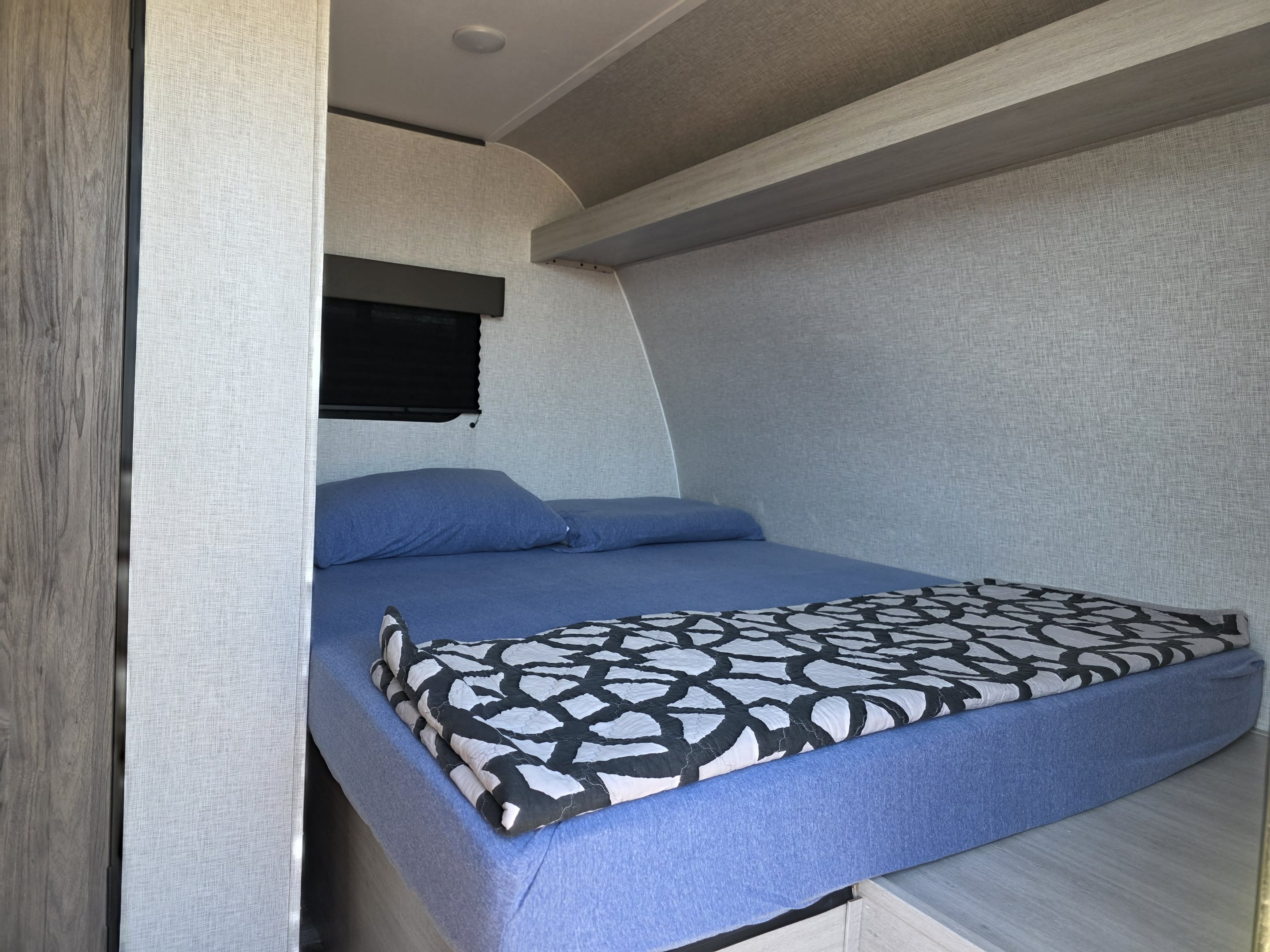 Cozy RV rental bedroom with a comfy bed, blue sheets, patterned comforter, and overhead storage, perfect for a restful sleep.. CrossRoads Zinger ZR18QB26 2026