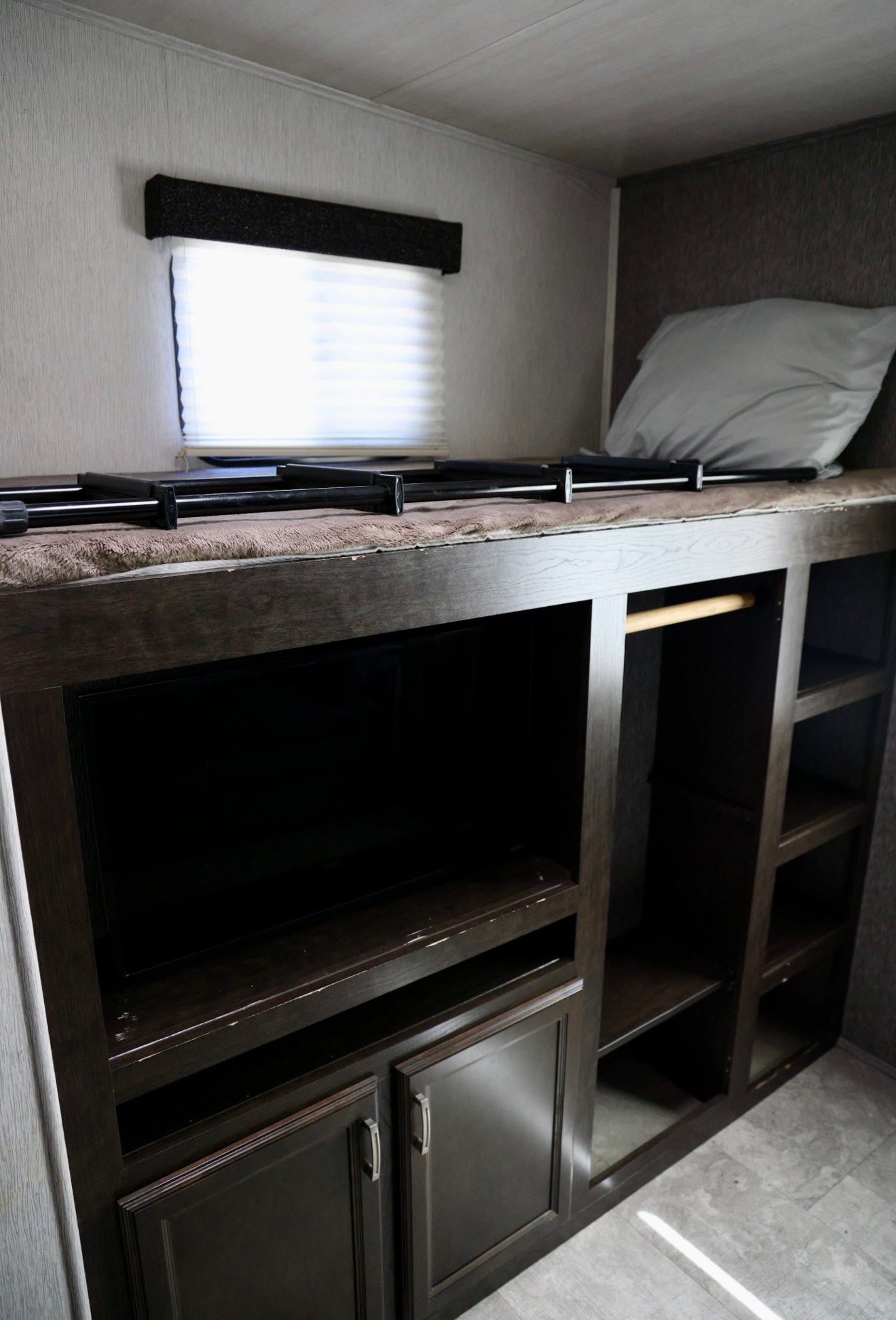 This RV rental features a bunk bed with safety rails above a TV and storage cabinets, providing a compact sleeping and media area.. Heartland RVs Pioneer 2019