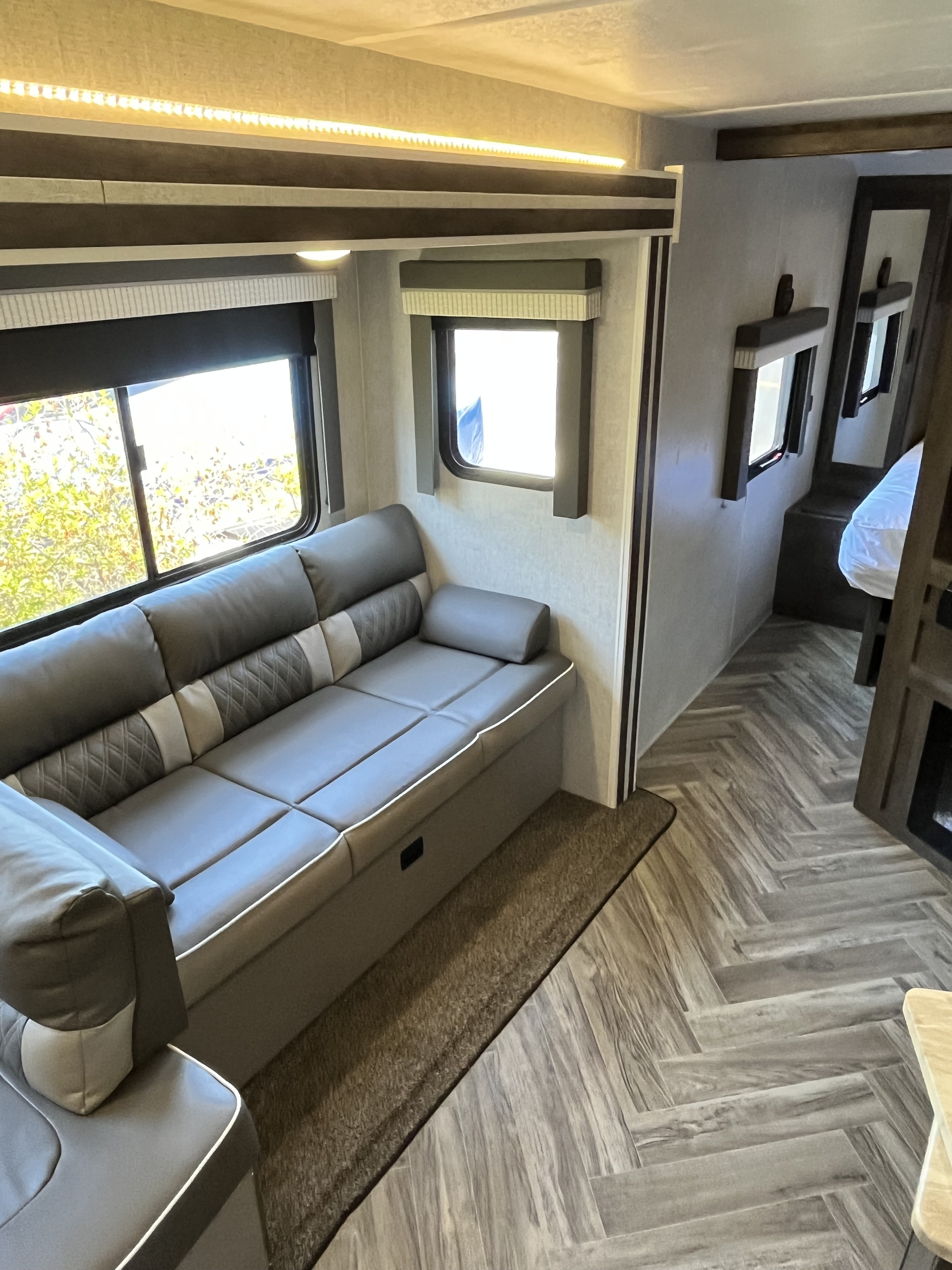Inside a stylish RV rental: gray sofa, herringbone floor, ample windows, and ambient lighting in the main living space.. Forest River Wildwood 2021