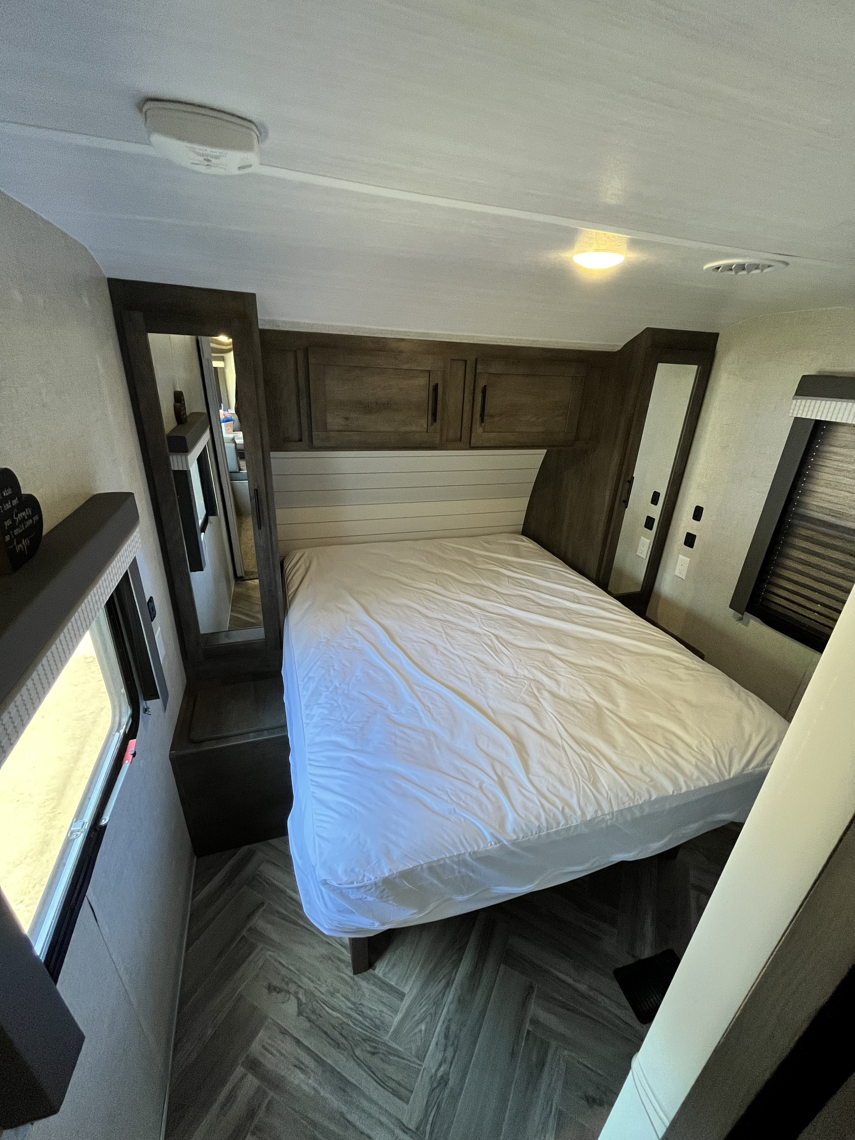 RV rental bedroom interior with white bed, wood cabinets, mirrors, and herringbone flooring, offering a compact space.. Forest River Wildwood 2021