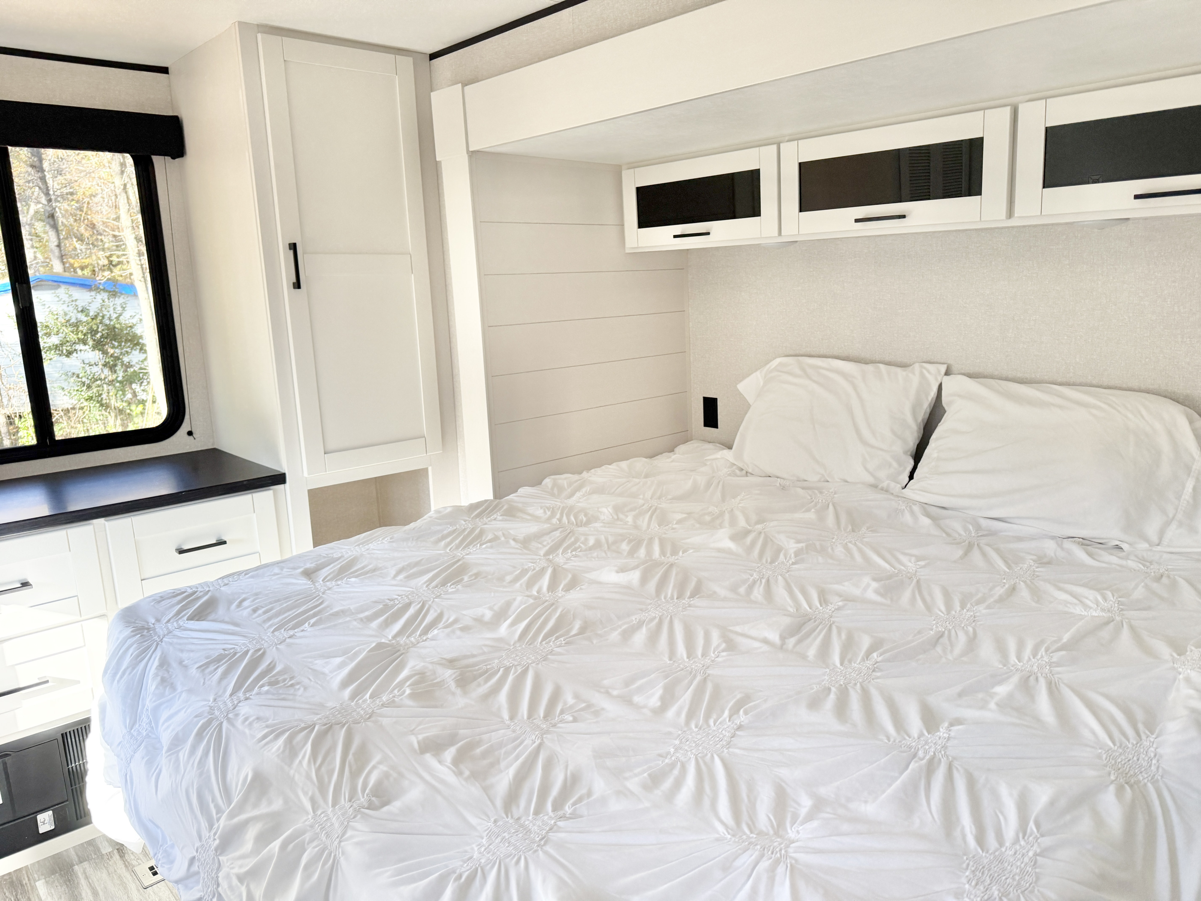 Bright and modern RV rental bedroom featuring a clean white bed, overhead cabinets, shiplap accent wall, and window view.. Jayco Jay Flight SLX 380DQS 2026