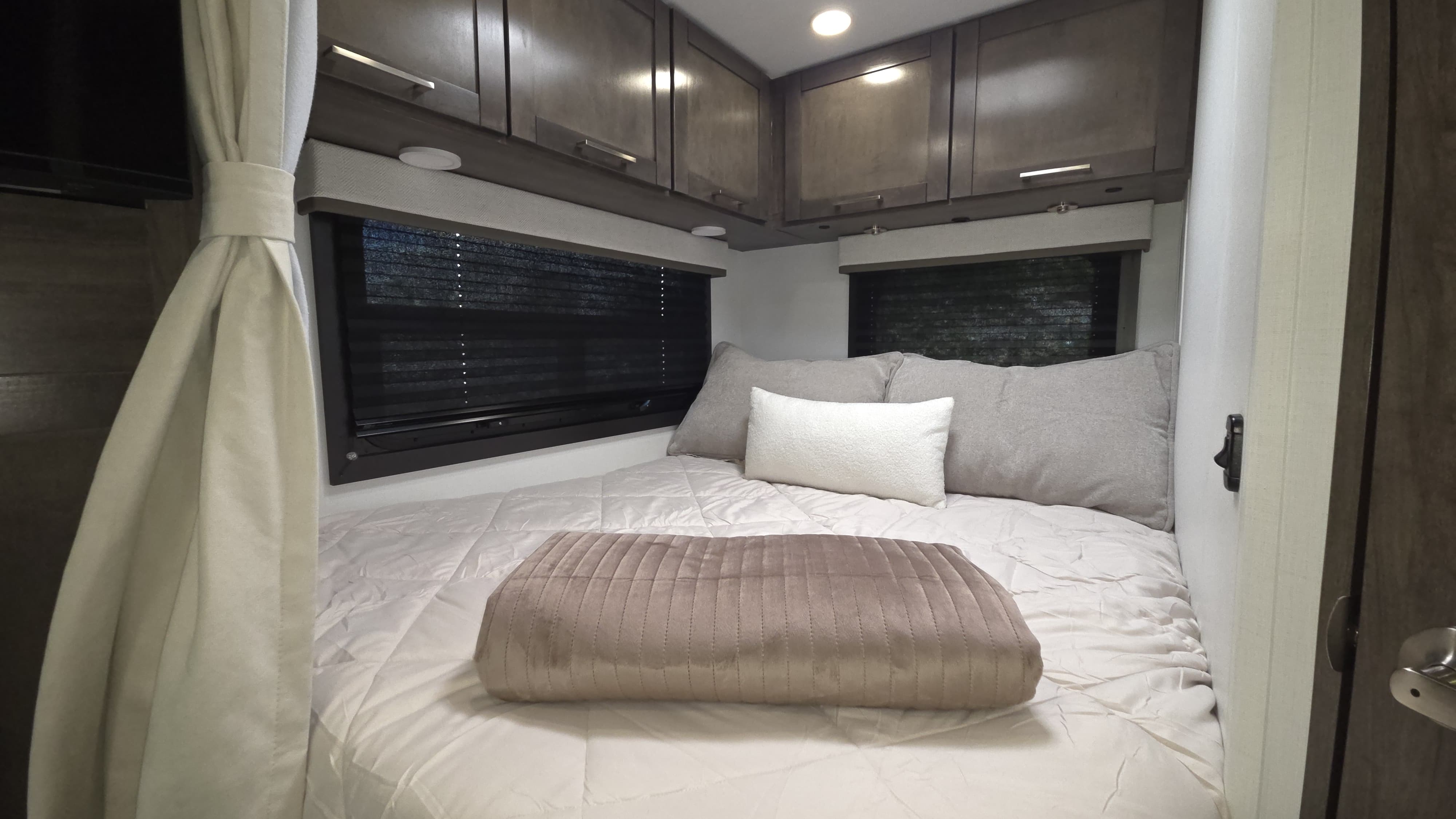 Cozy RV rental bedroom with a neatly made bed, dark overhead cabinets, and window blinds for privacy.. Entegra Coach Odyssey 25R 2026