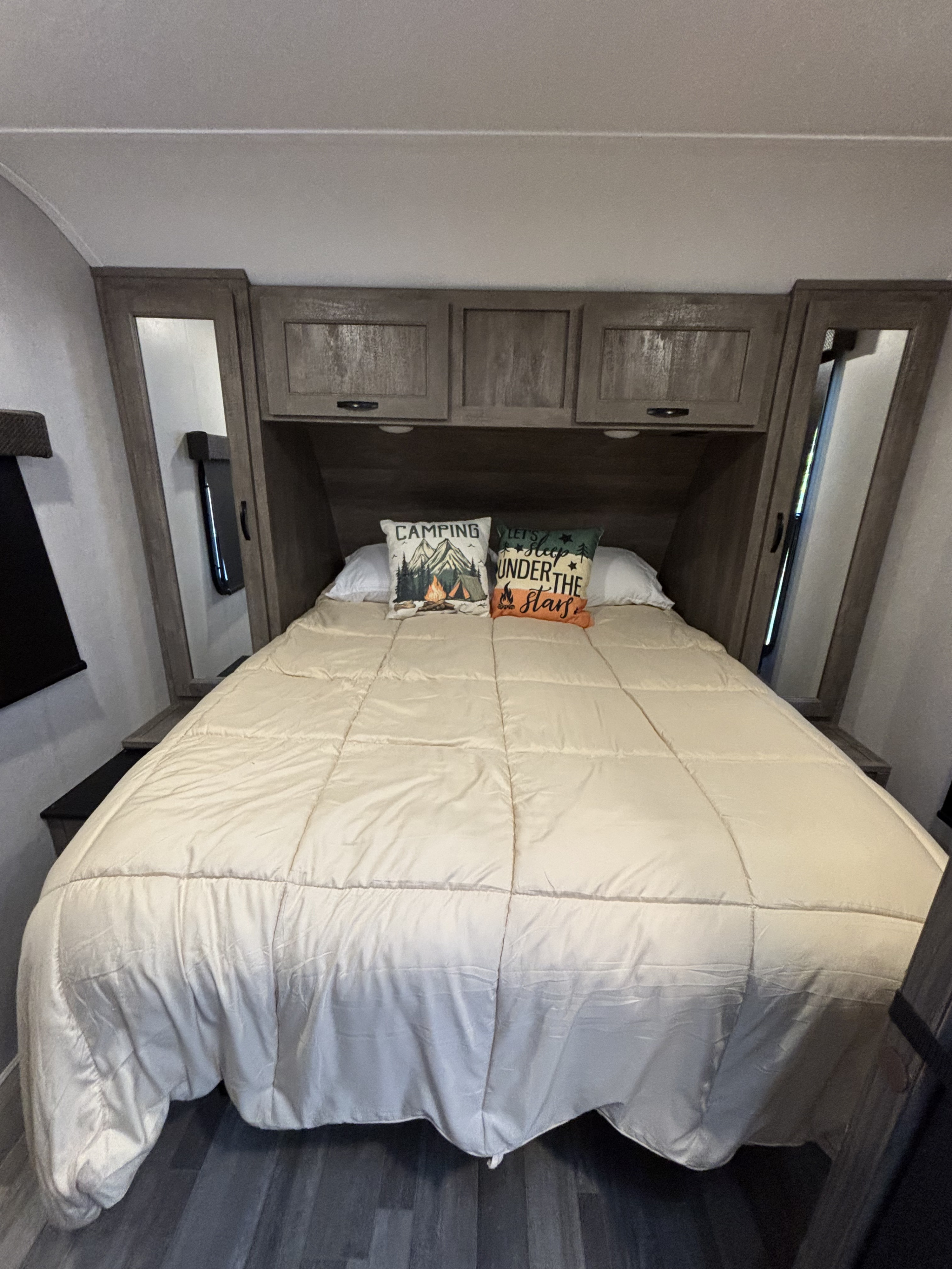 Cozy RV rental bedroom featuring a queen bed with camping pillows, overhead storage, and mirrored wardrobes.. Forest River Vibe 2021