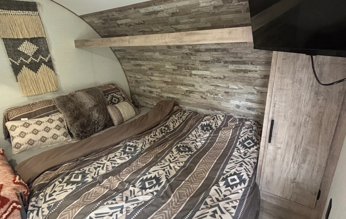 Cozy RV rental bedroom featuring southwestern-patterned bedding, faux wood paneling, decorative wall hangings, and a TV.. Gulf Stream Enlighten Super Lite 2025