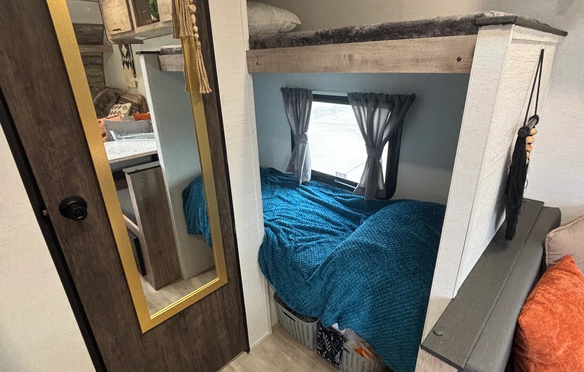 RV rental: Cozy bunk beds with a window, dressed in a blue blanket, beside a door with a full-length mirror.. Gulf Stream Enlighten Super Lite 2025