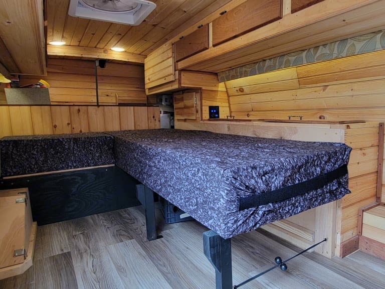 Cozy RV rental camper van interior featuring a modular L-shaped bed/seating, wood paneling, and ceiling fan.. Gmc Savanna 2014