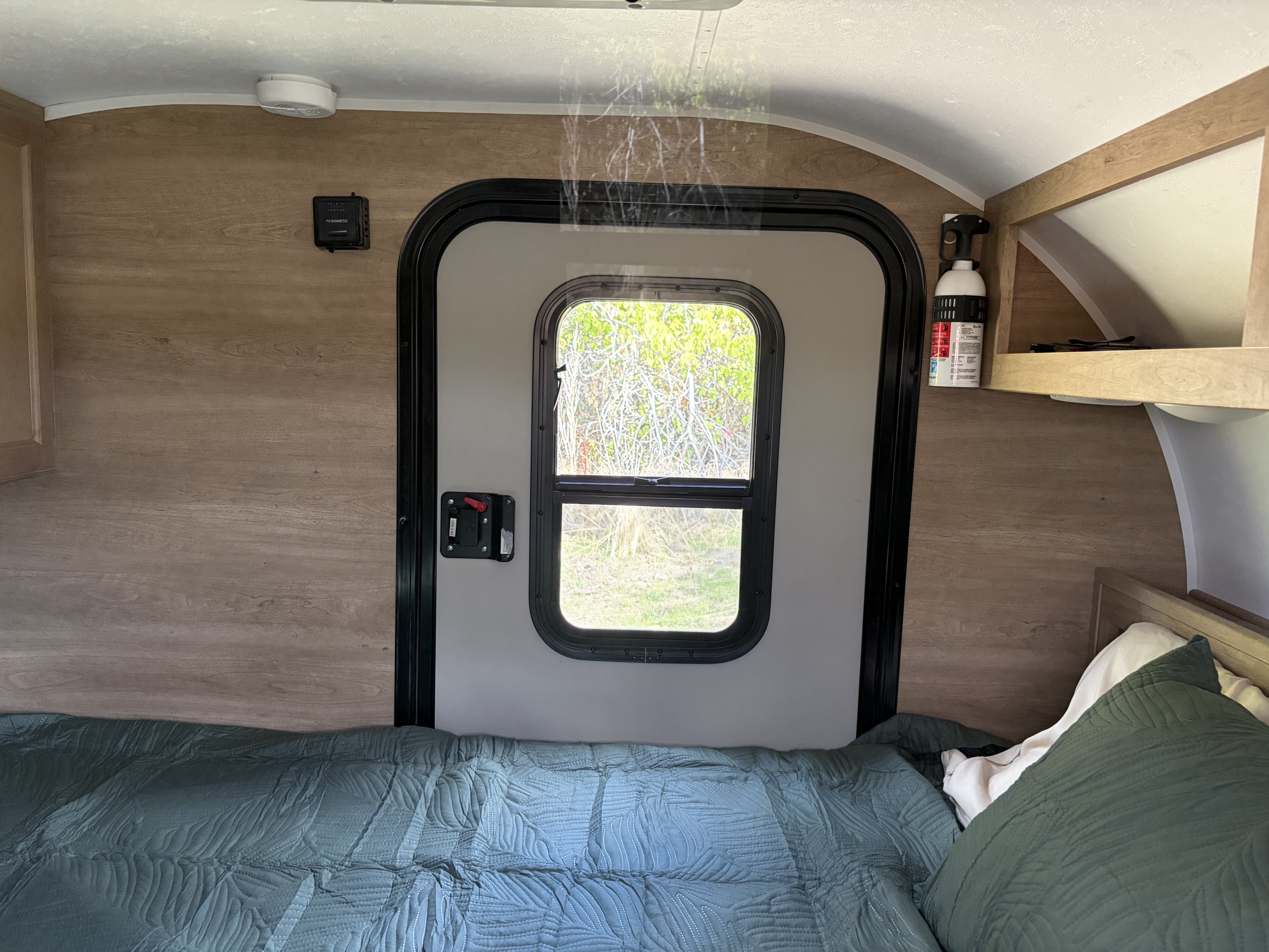 Cozy RV rental bedroom featuring a comfy bed, door with windows looking out to nature, a fire extinguisher, and climate controls.. Braxton Creek Braxton Creek Trailer 2020