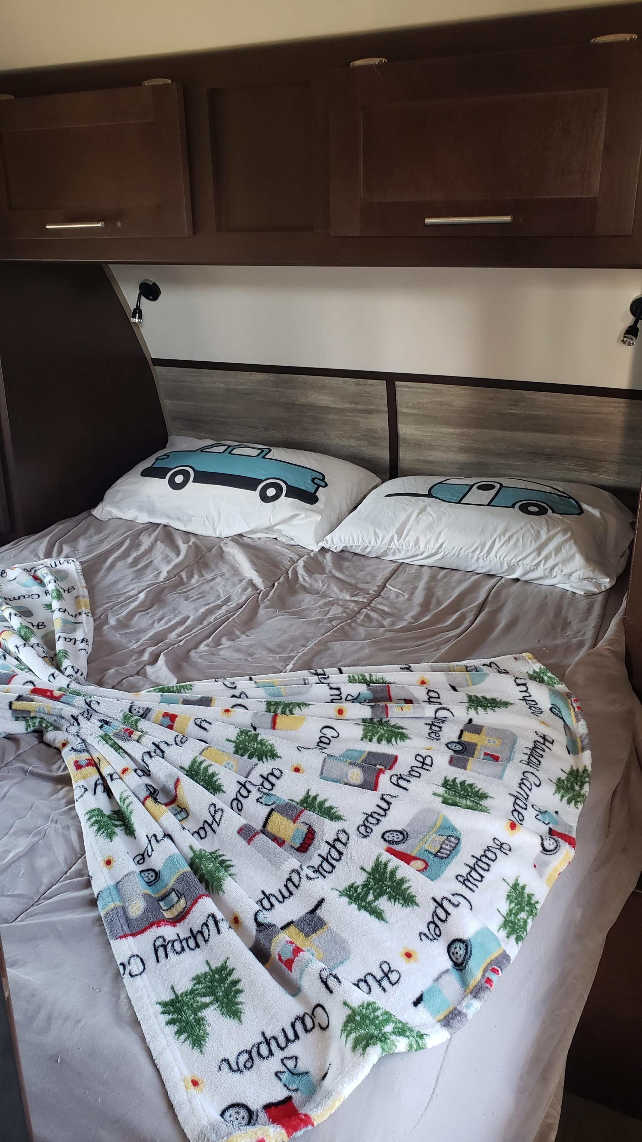 Cozy RV rental bedroom featuring car & camper pillows, a "Happy Camper" blanket, and overhead storage for a comfy stay.. Forest River Cherokee Grey Wolf 2017