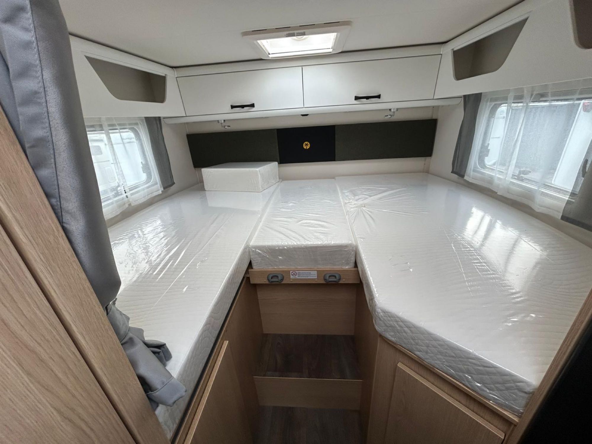 Bright **rv rental** interior: a bedroom with new U-shaped beds, plastic-wrapped mattresses, overhead storage, and windows.. Sunlight T66S 2026