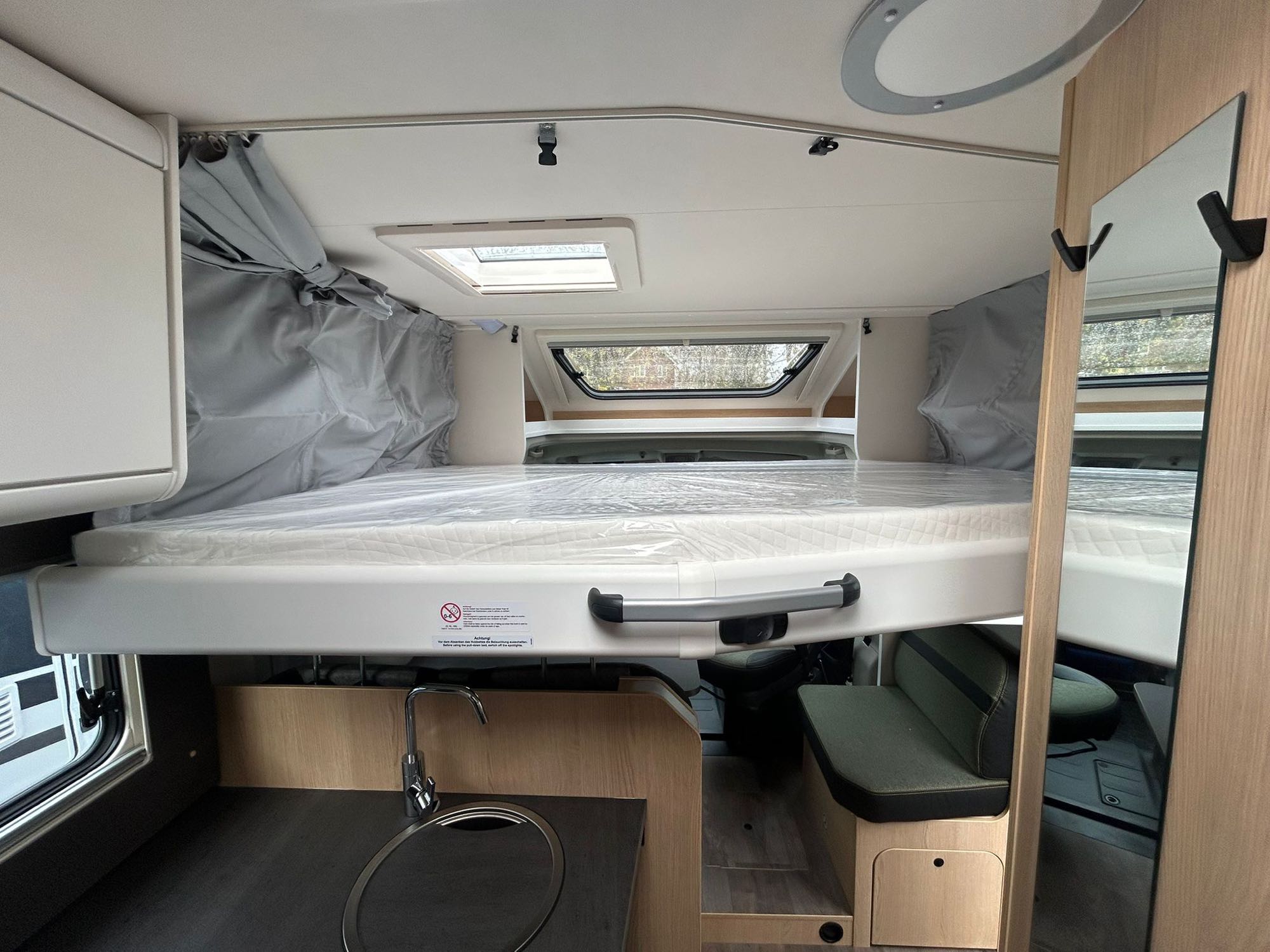 Bright RV rental interior featuring an overhead bed with a new mattress, a compact kitchen sink, and comfortable seating.. Sunlight T66S 2026