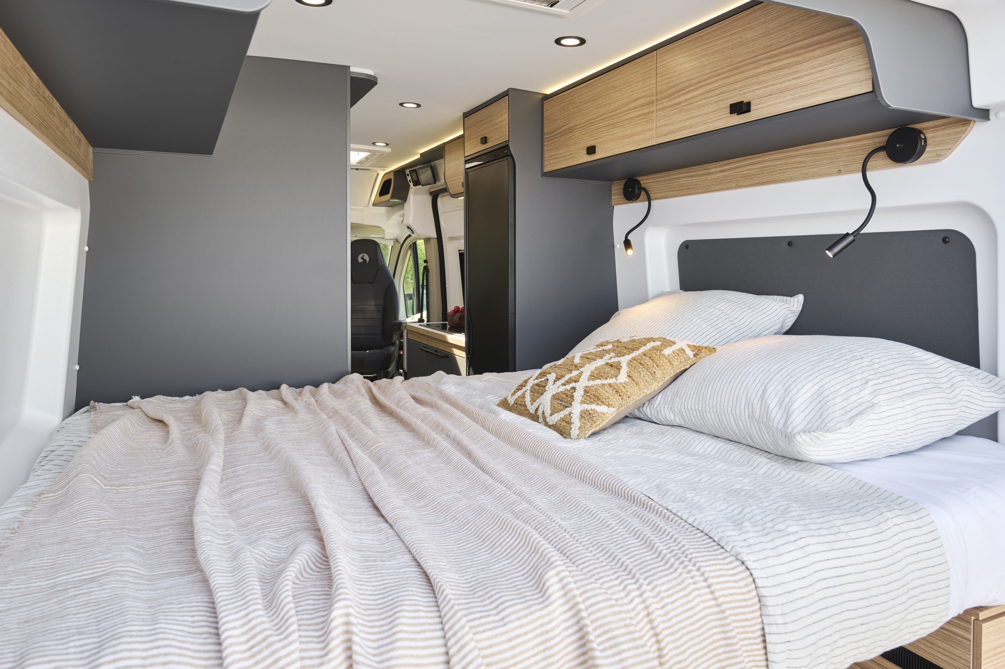 Sleek rv rental interior: a bright, modern bedroom with a cozy bed, striped bedding, overhead cabinets, and reading lights.. BAVARIA K600G 2026