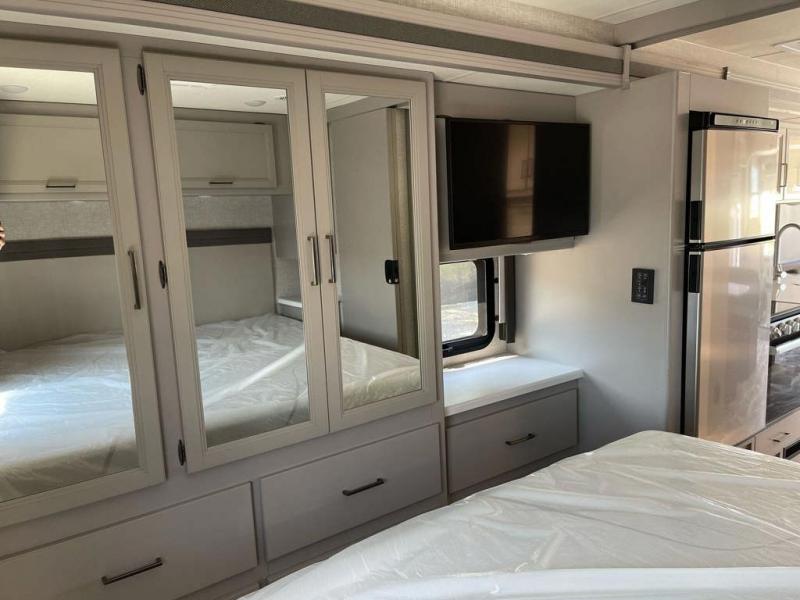 Explore this modern RV rental's bedroom with mirrored wardrobes, TV, and adjacent kitchen area for comfortable travel.. Thor Windsport 2023