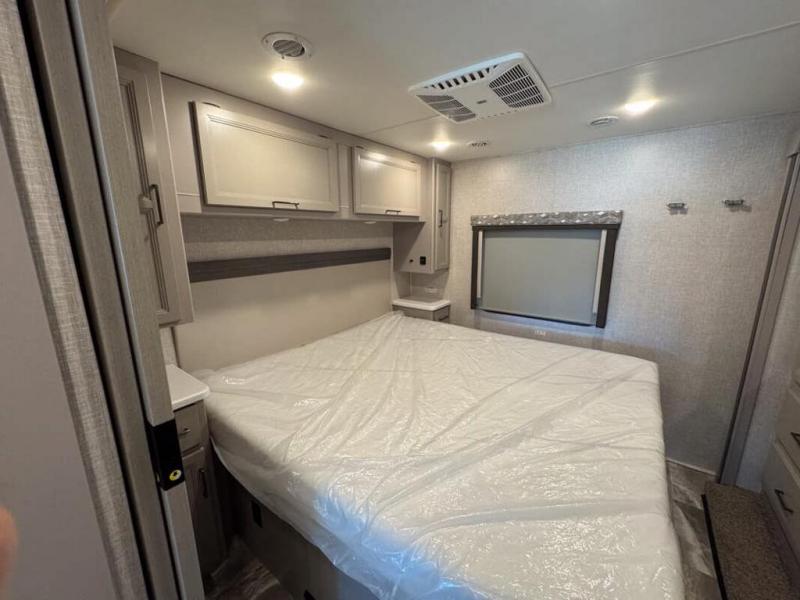 RV rental bedroom interior: Features a large bed with plastic cover, overhead cabinets, a window, and an AC unit.. Thor Windsport 2023