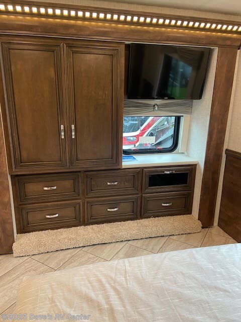RV rental bedroom with dark wood cabinetry, multiple drawers, wall-mounted TV, and window displaying another RV outside.. Bay Star Bay Star Motorhome 2022