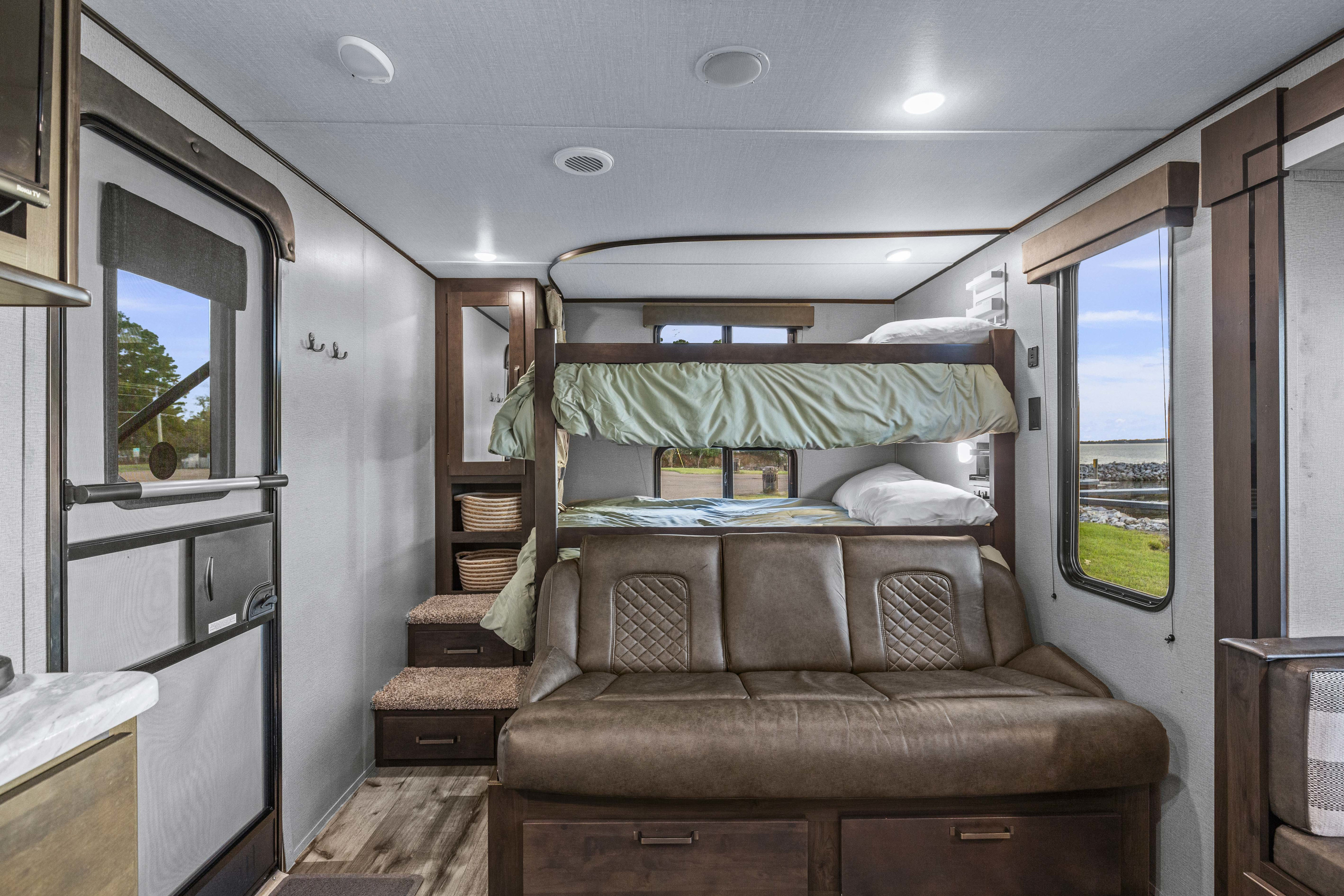 RV rental bunkhouse interior with a brown sofa, bunk beds, and an entrance door, ideal for family trips.. Grand Design Transcend Xplor 2023