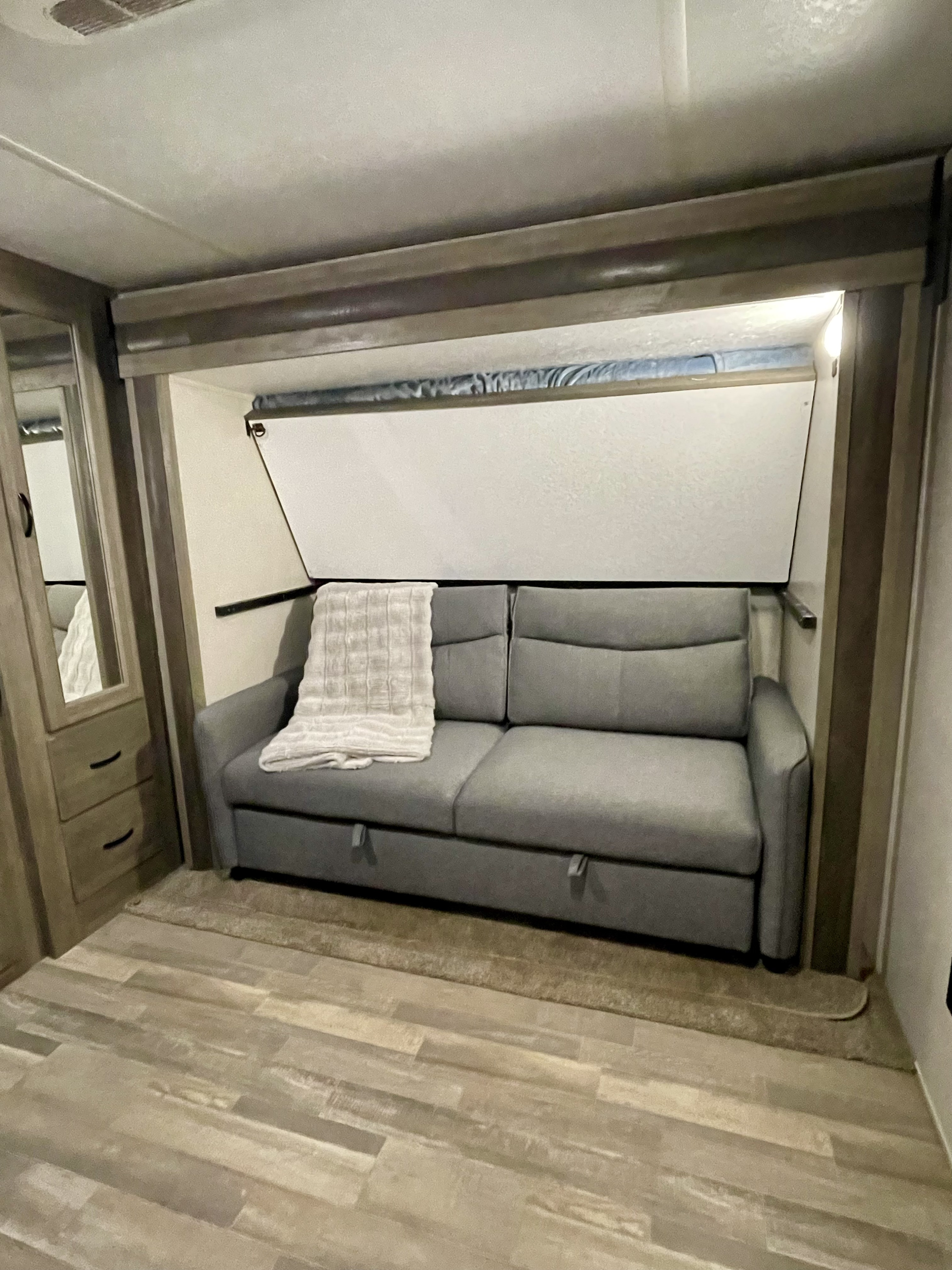 Modern RV rental interior with a gray pull-out sofa bed and blanket, built-in lighting, and wood-look flooring.. Forest River Vibe 2020