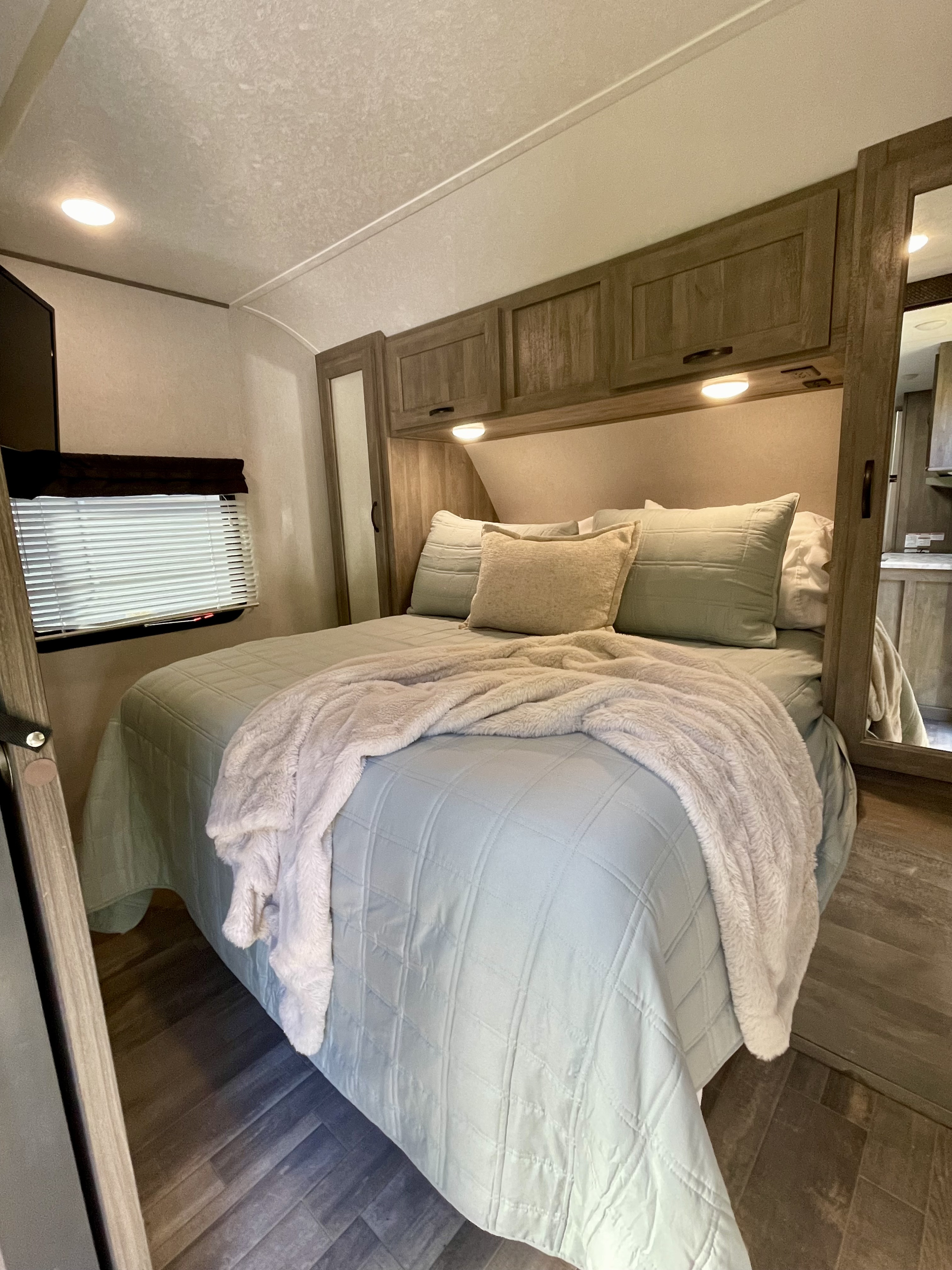 This welcoming RV rental bedroom offers a comfortable bed with light blue bedding, overhead storage & bright lights.. Forest River Vibe 2020
