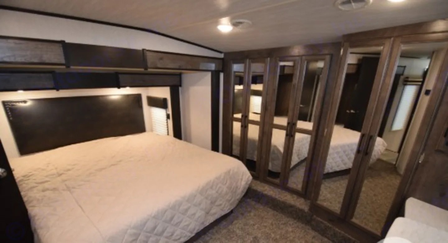 Cozy RV rental bedroom with a comfortable bed, overhead storage, and mirrored closet for your travel needs.. Heartland RVs Cyclone Toy Hauler 2020