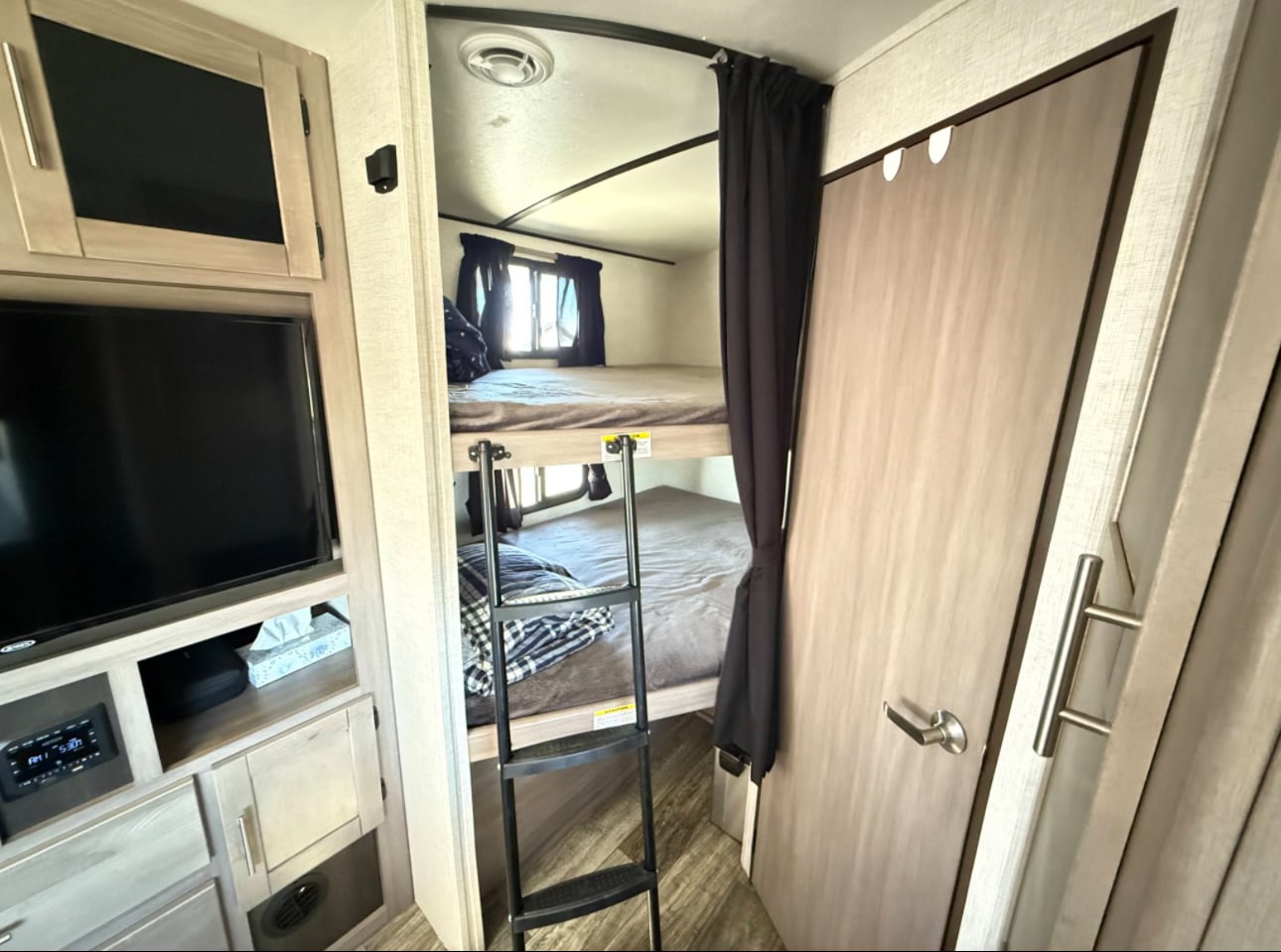 Cozy RV rental interior: bunk beds with ladder & privacy curtain next to an entertainment center with TV.. Crossroads RV Sunset Trail Super Lite 2021