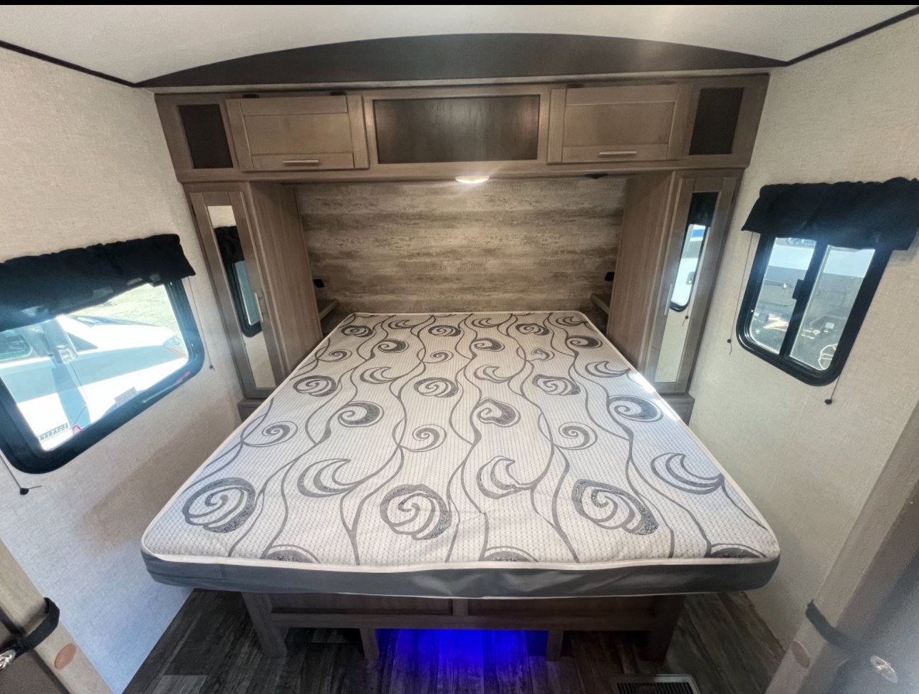 Spacious RV rental bedroom featuring a modern bed with patterned mattress, overhead storage, and dual windows.. Crossroads RV Sunset Trail Super Lite 2021