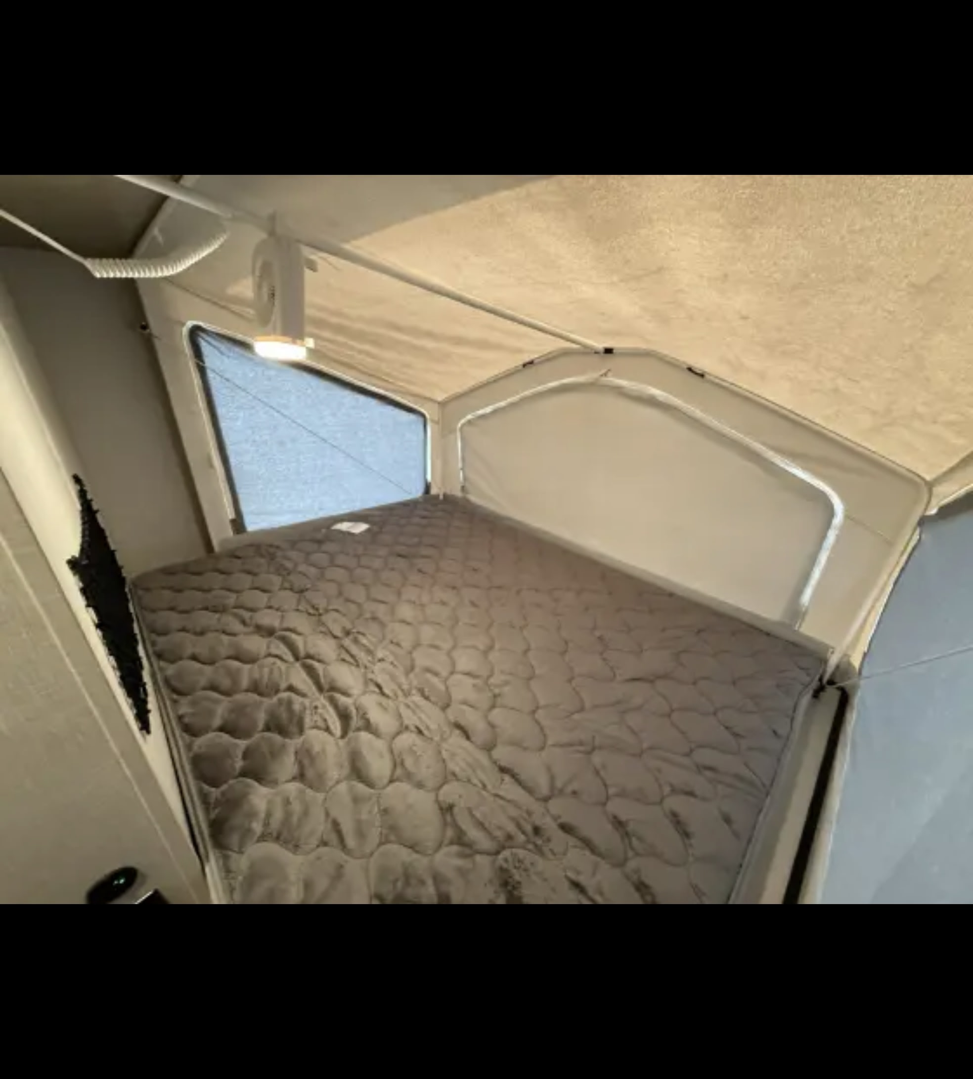 A comfortable sleeping area in an RV rental, showing a quilted gray mattress, a mesh window, and an overhead LED light.. Forest River Flagstaff Shamrock 2022