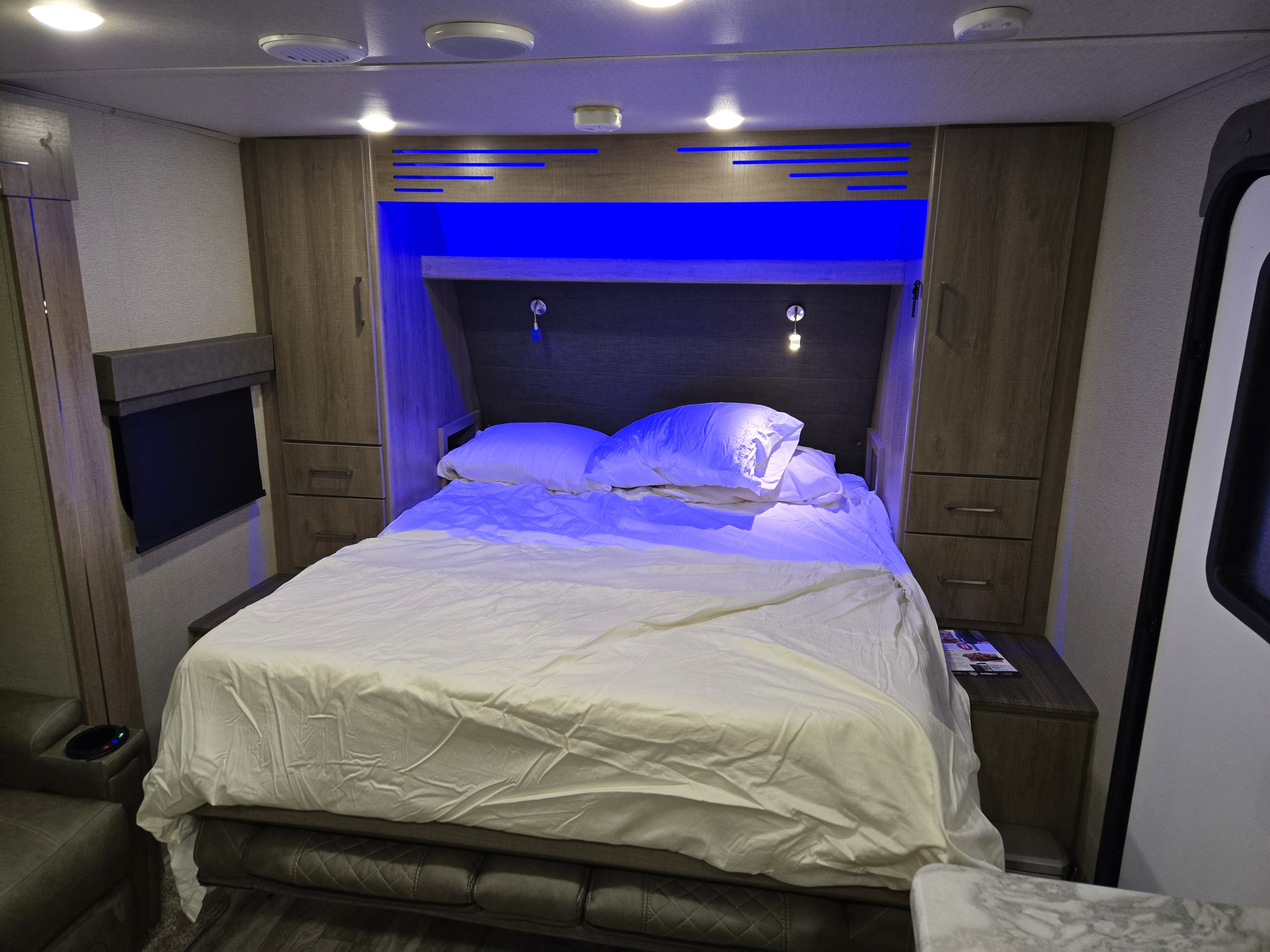 Cozy RV rental bedroom with blue accent lighting, a comfortable bed, and wood storage cabinetry for a relaxing journey.. Grand Design Imagine XLS 2022