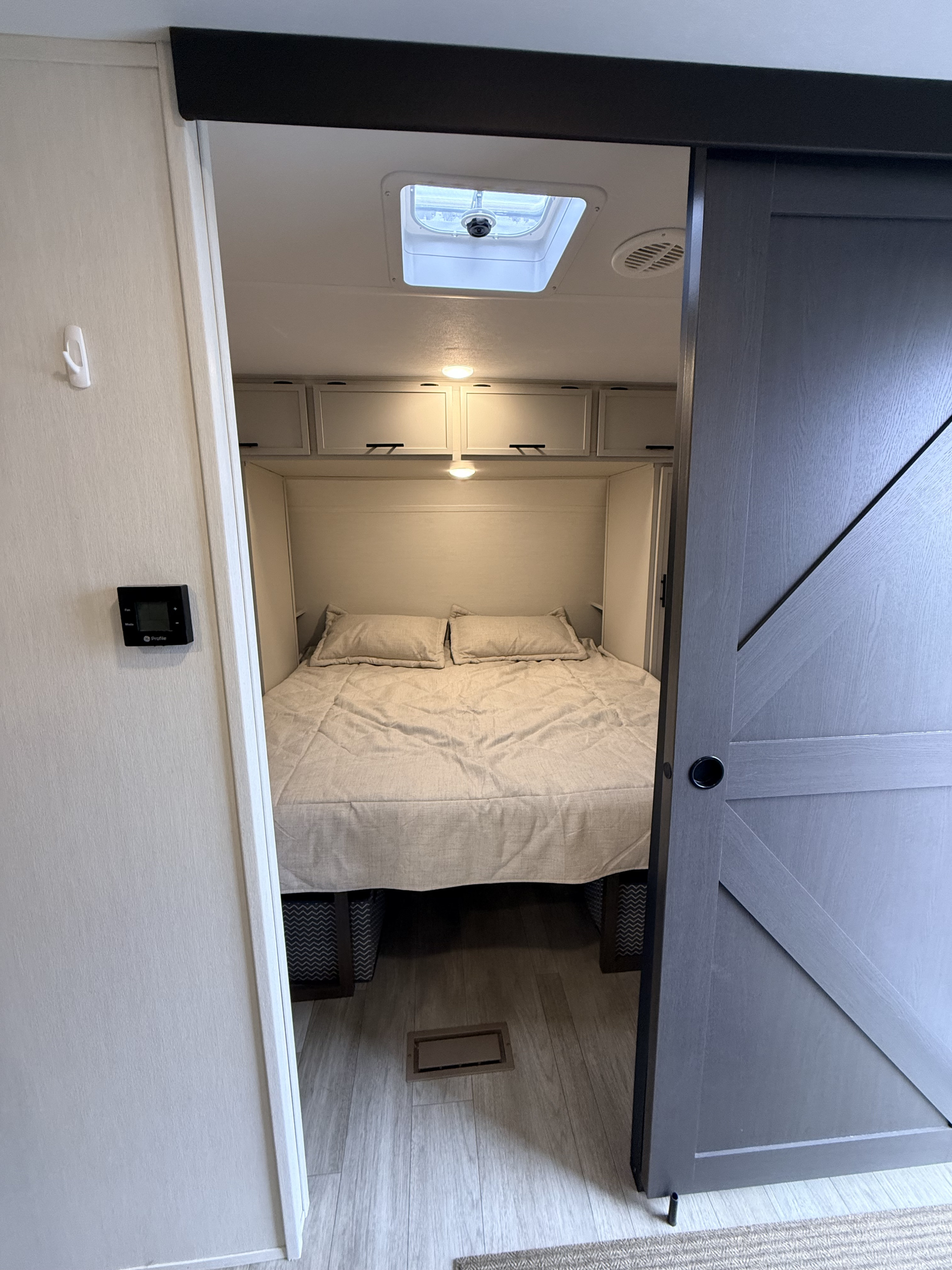 RV rental bedroom with a comfortable bed, overhead storage, ceiling vent, and stylish sliding barn door.. Forest River AVENGER 26DBS 2026