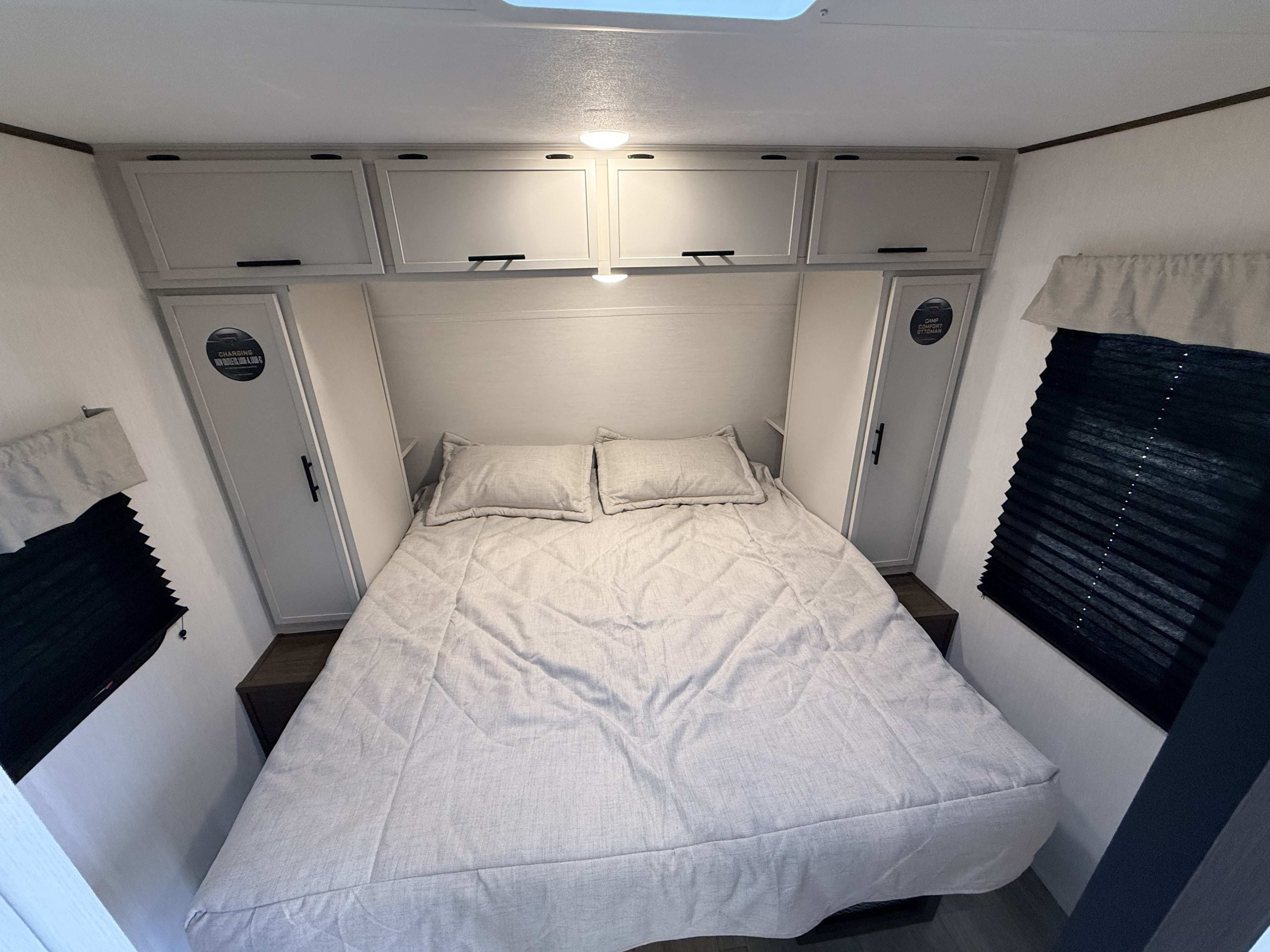 Cozy RV rental bedroom features a comfortable bed, overhead cabinets, side wardrobes with charging outlets, and window blinds.. Forest River AVENGER 26DBS 2026