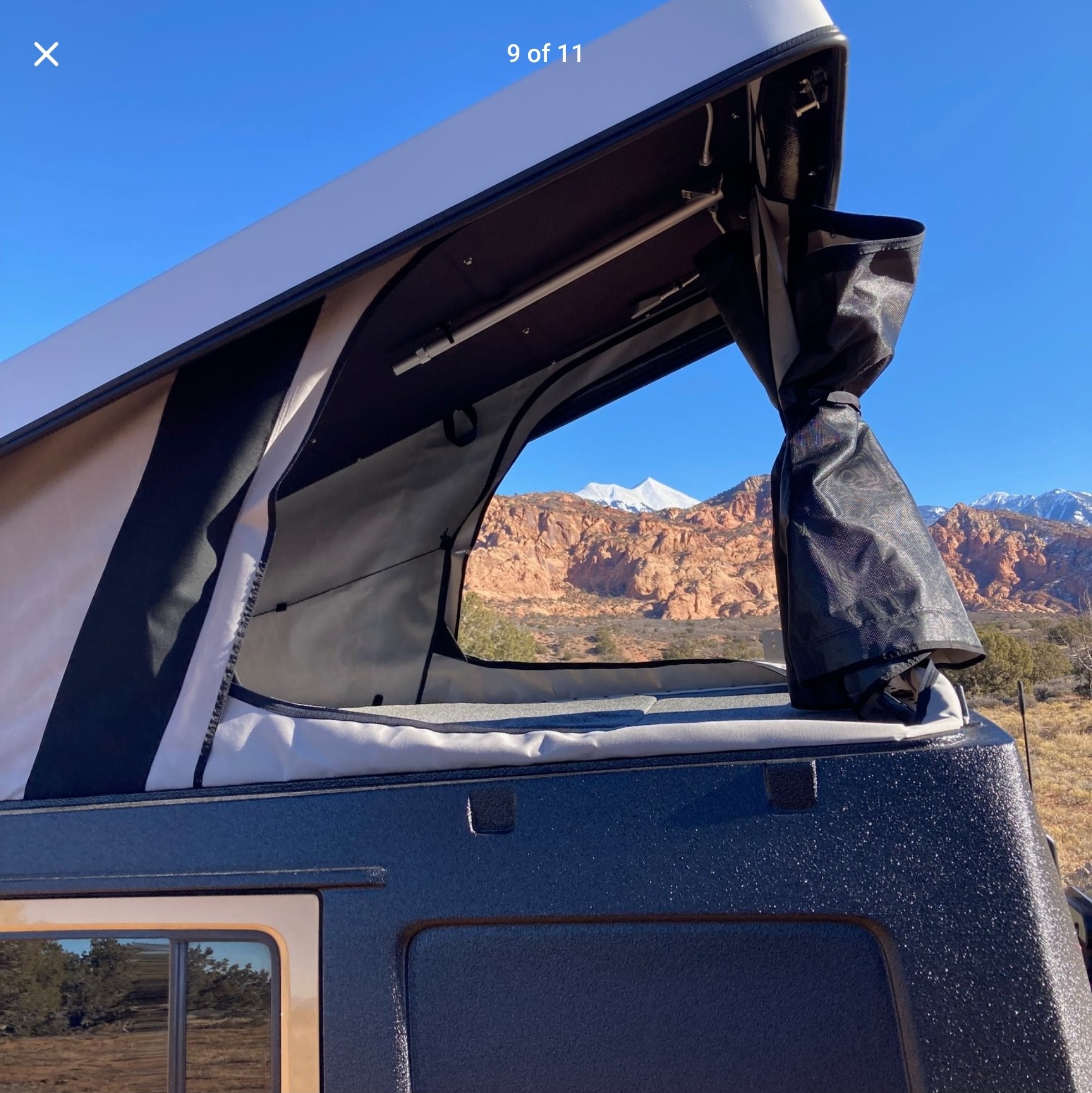 Inside an RV rental pop-top camper, revealing a breathtaking view of red rock mountains and snow-capped peaks.. Jeep Wrangler 2014